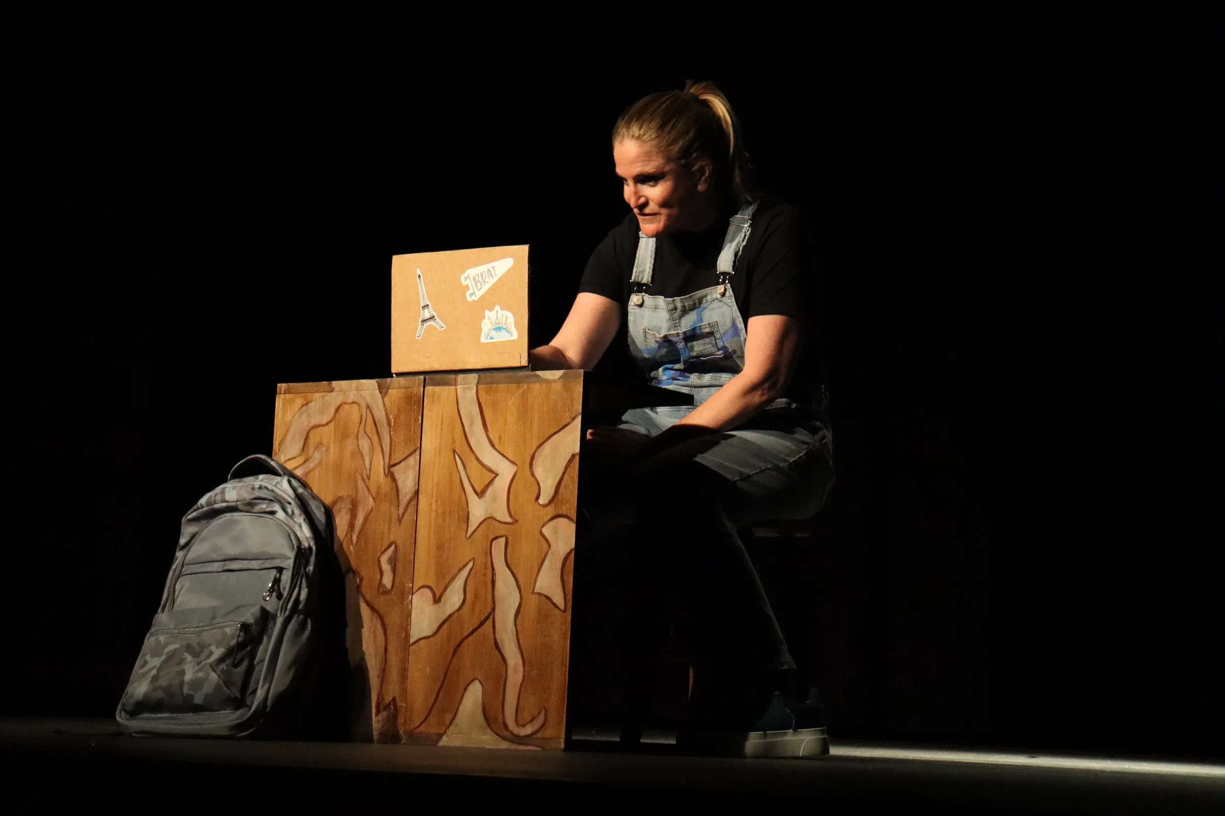 Close up of actress using a cardboard laptop on a hand painted furniture piece in the world premiere play “BRAT” by Wendy Maples