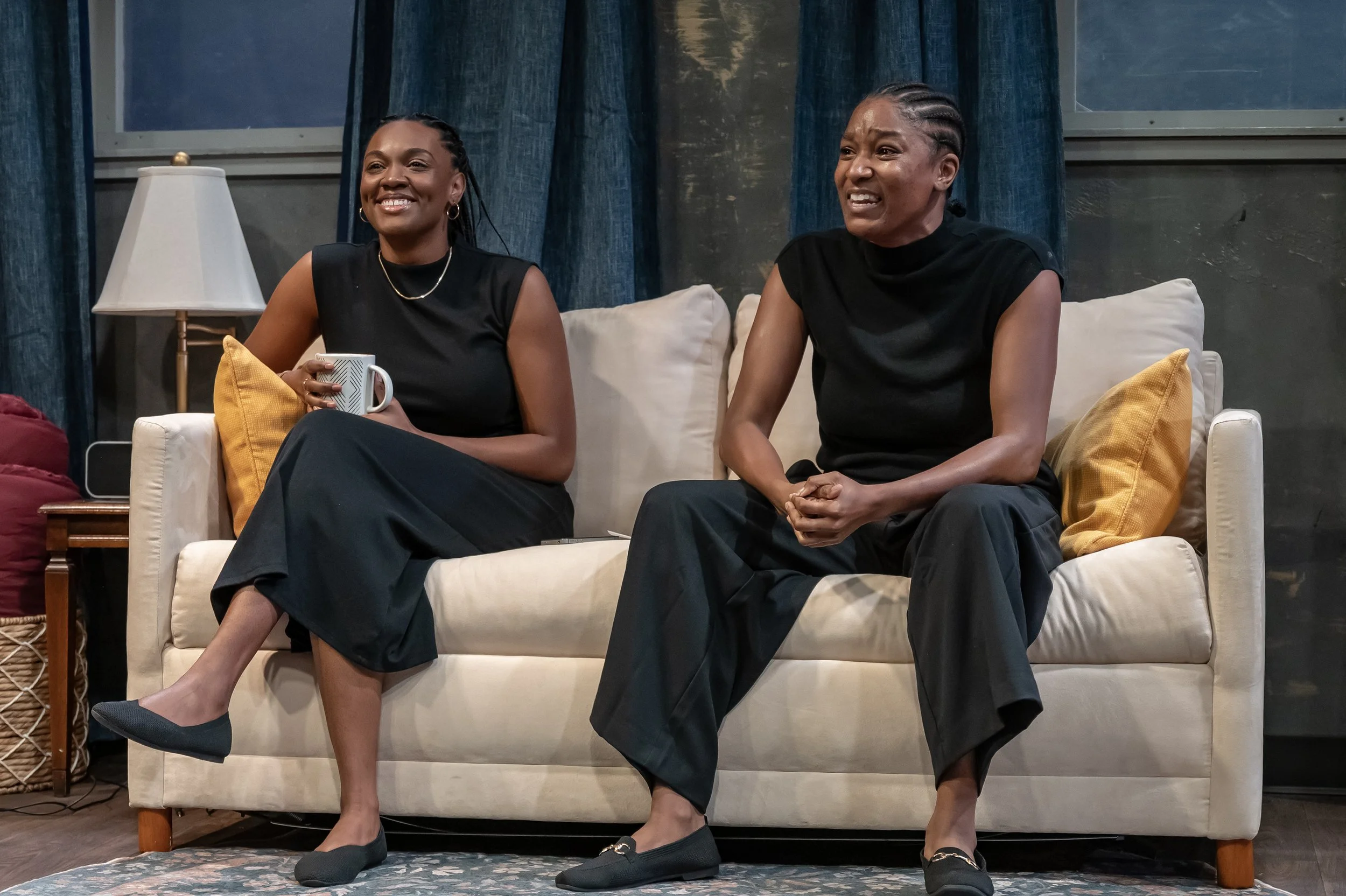 Mina and Sade sitting on the couch in the play “Furlough’s Paradise” by A.K. Payne