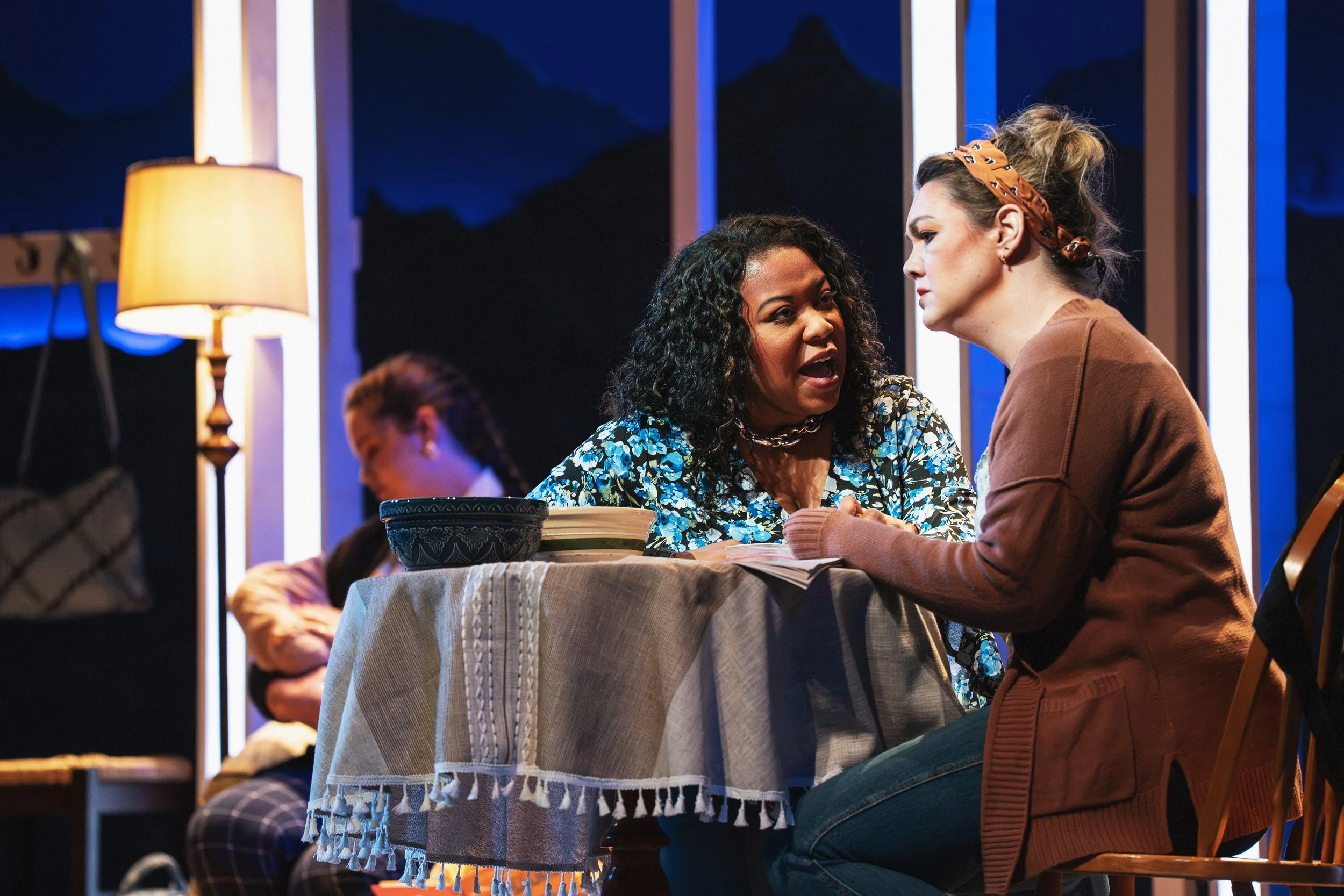 A discussion over a kitchen table in the opera “The Knock”