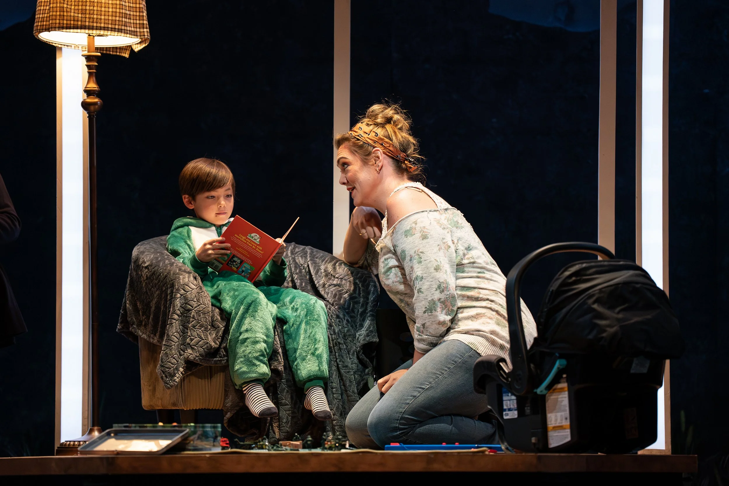 A child reading in an armchair with his mother in the opera “The Knock”