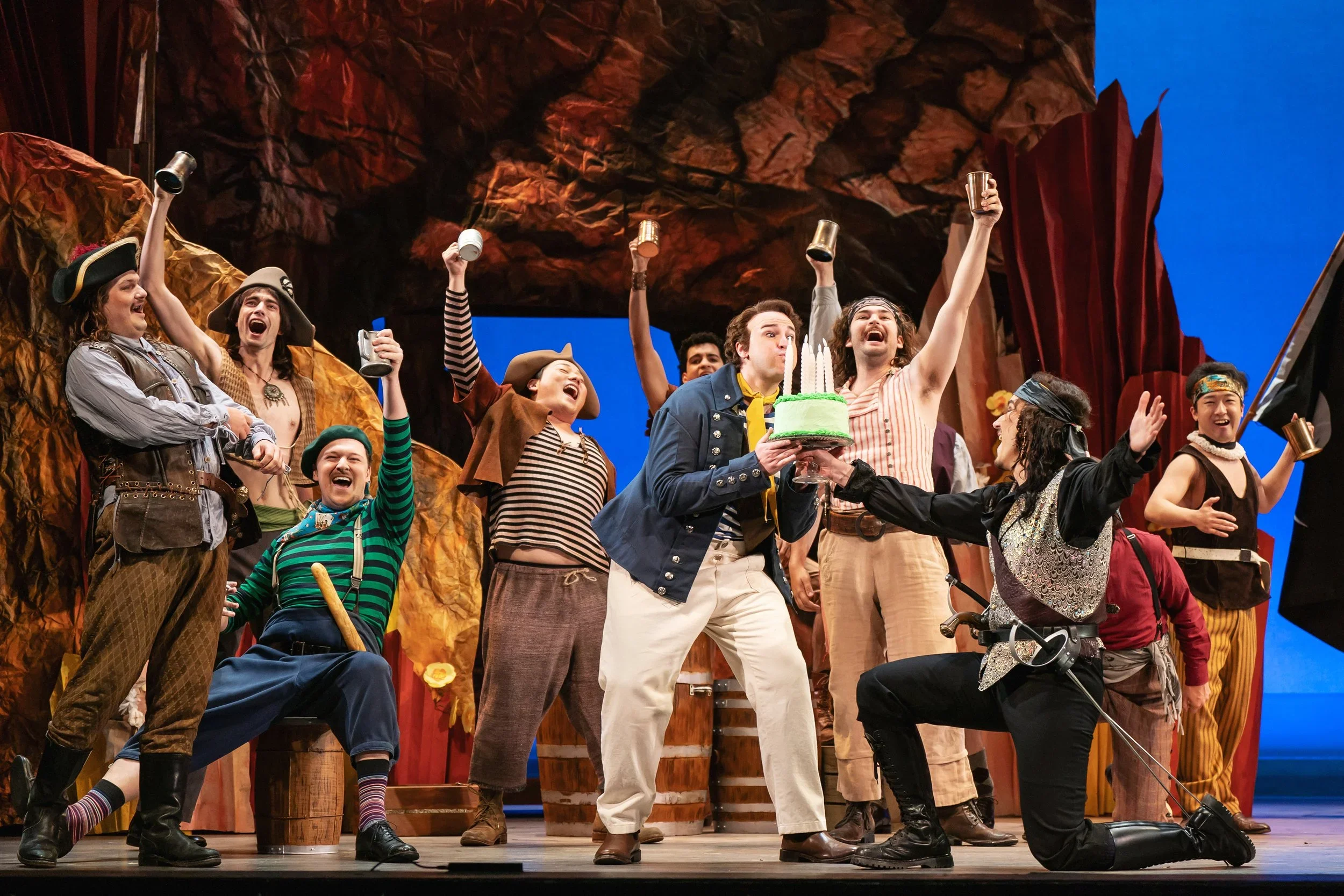 Party shot of pirates with mugs of beer and a birthday cake with controllable candles in the opera “The Pirates of Penzance”