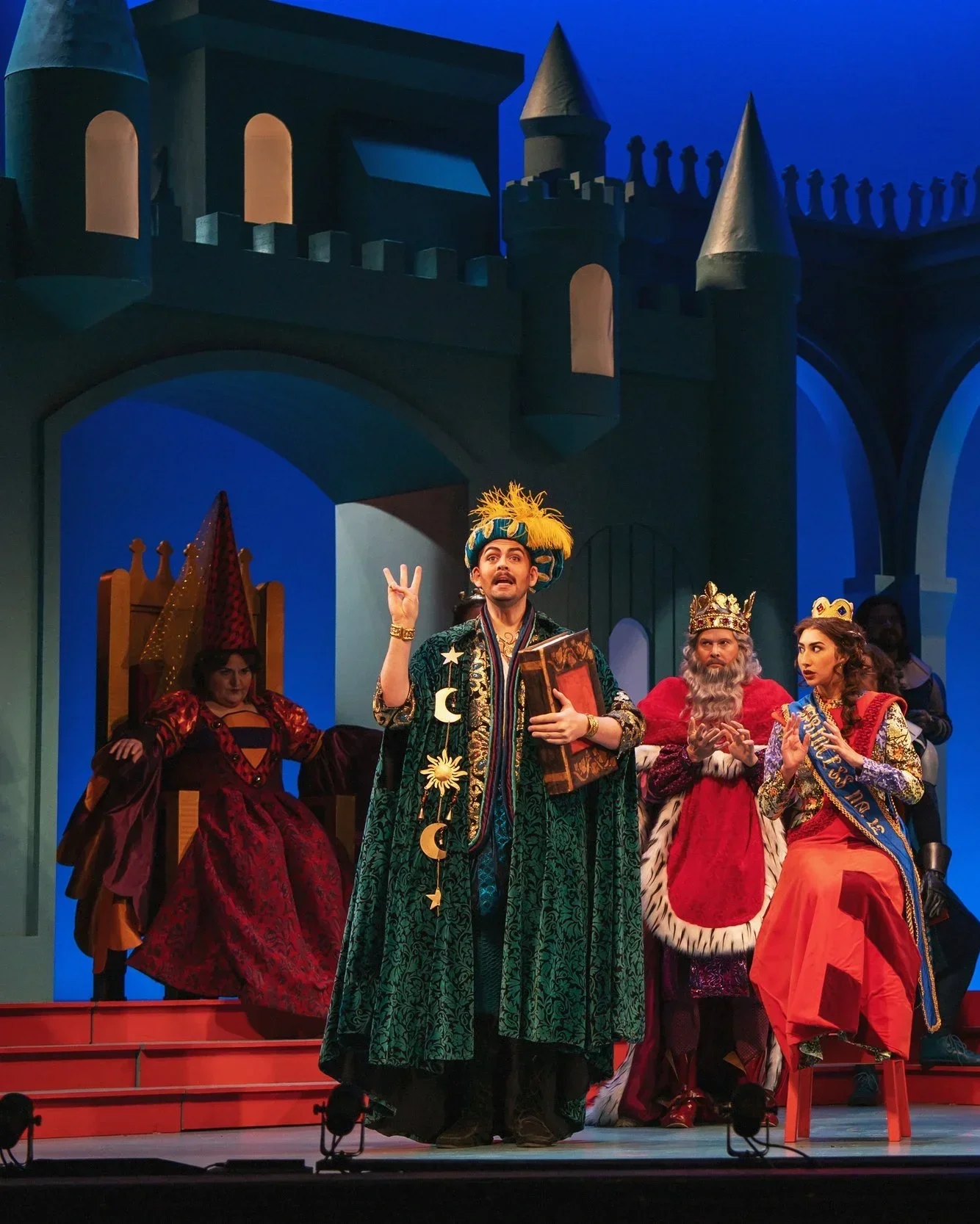 The wizard holding a large spell book in the opera “Once Upon a Mattress”