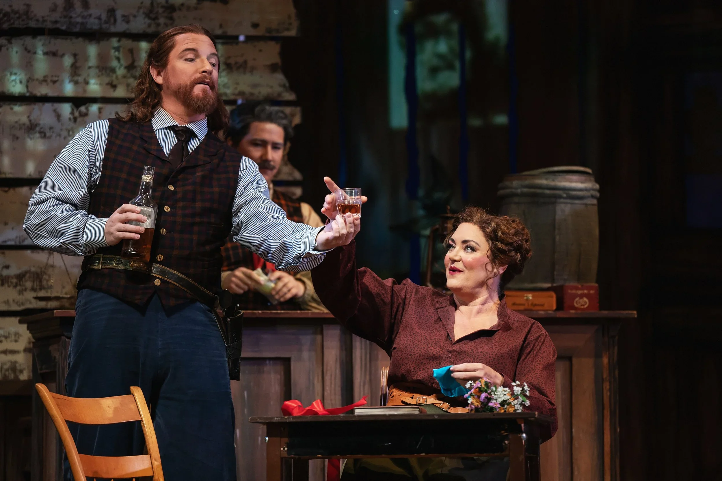 Close up of drinkers in the bar in the opera “La Fanciulla del West,” featuring whiskey, flowers, and more props