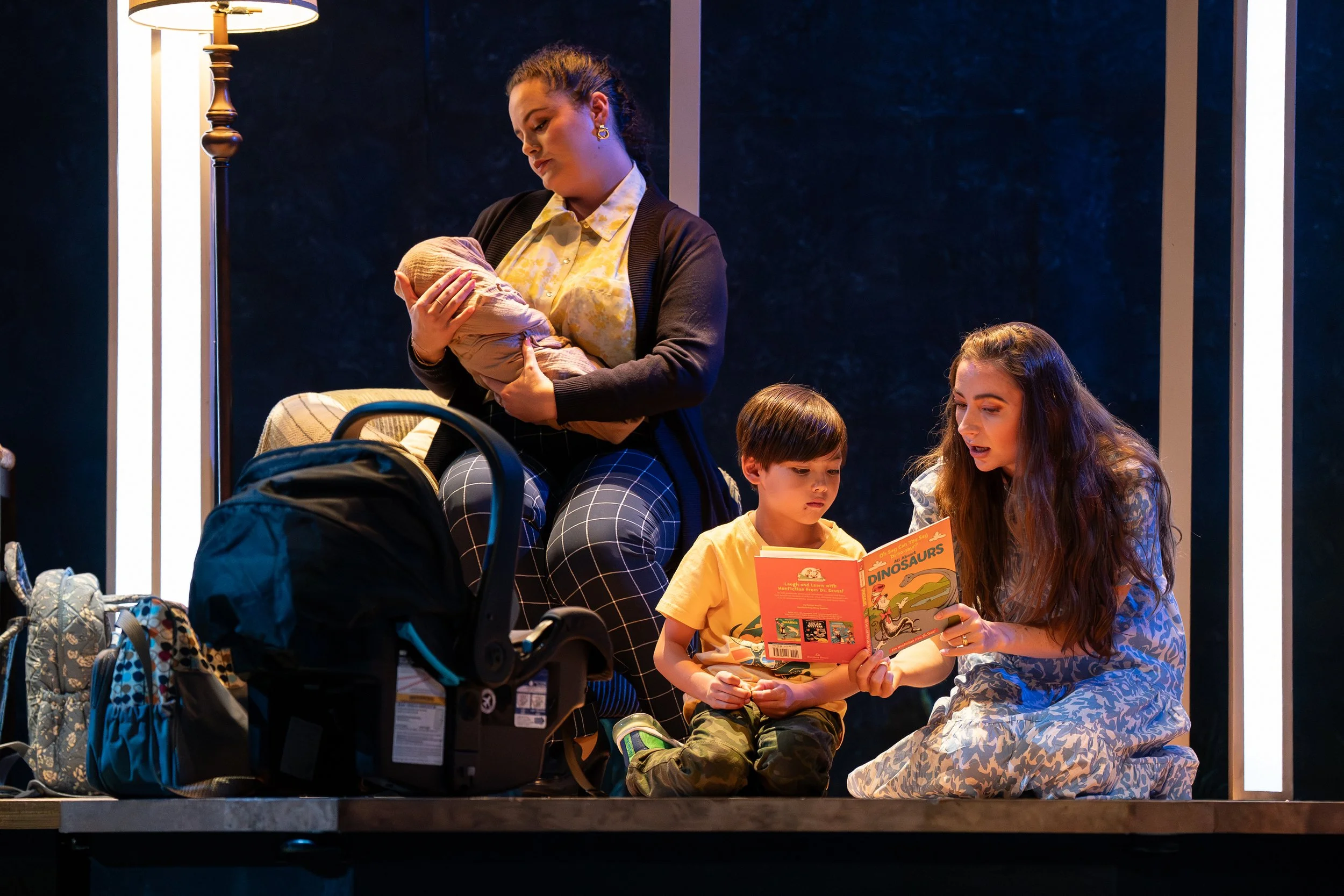 Characters holding a baby and reading to a small child in the opera “The Knock”