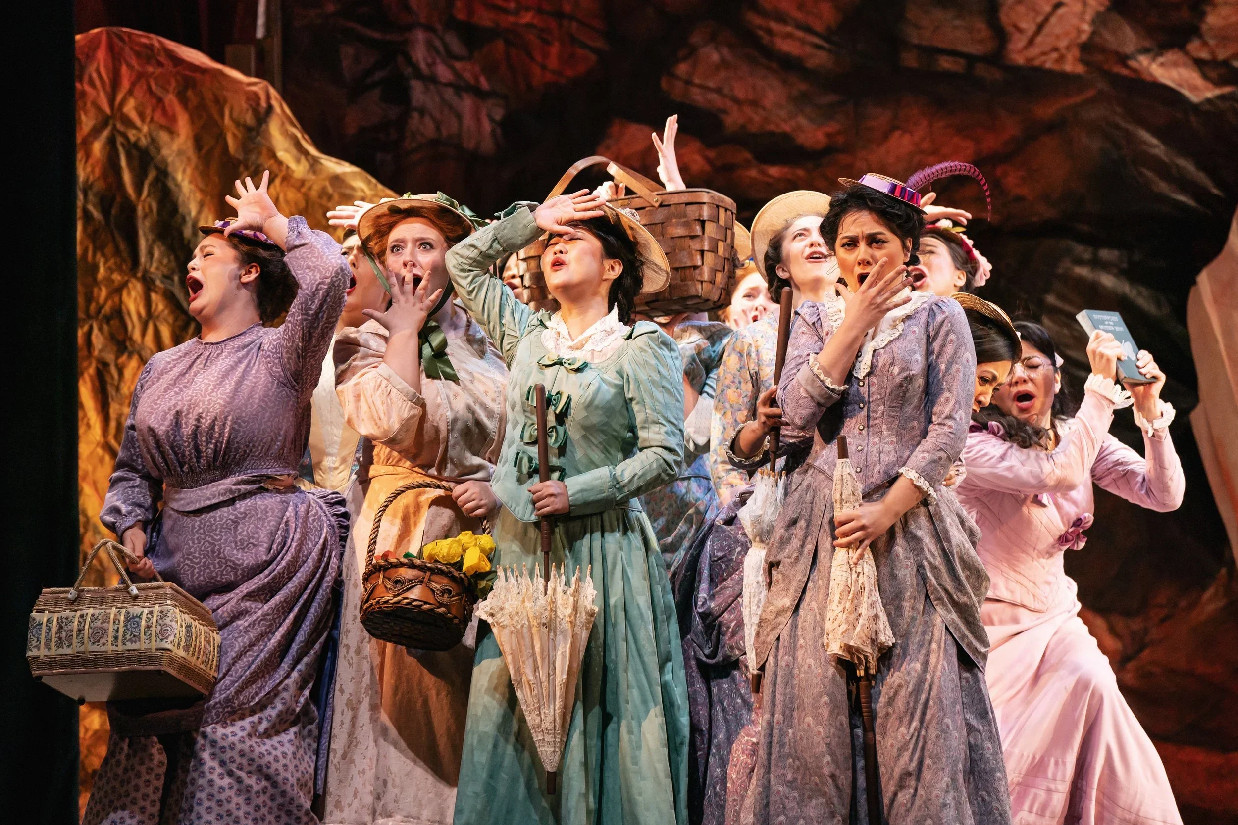Women with baskets, paper flowers, books, and more acting aghast in the opera “The Pirates of Penzance”