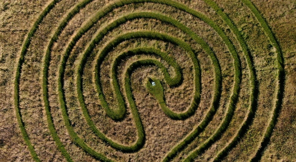 An aerial view of a heart-shaped maze made of shrubs in a grassy field, with a small white vehicle at the center. The Fields at Rootspring, Annandale, MN.