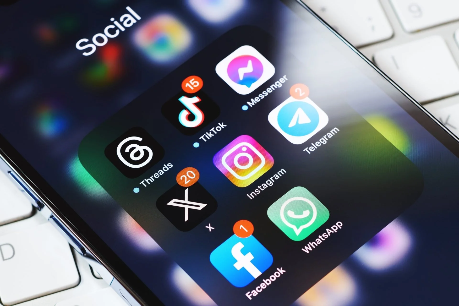 Close-up of a smartphone screen displaying social media app icons including TikTok, Messenger, Telegram, Instagram, WhatsApp, Facebook, and others, placed next to a white keyboard.