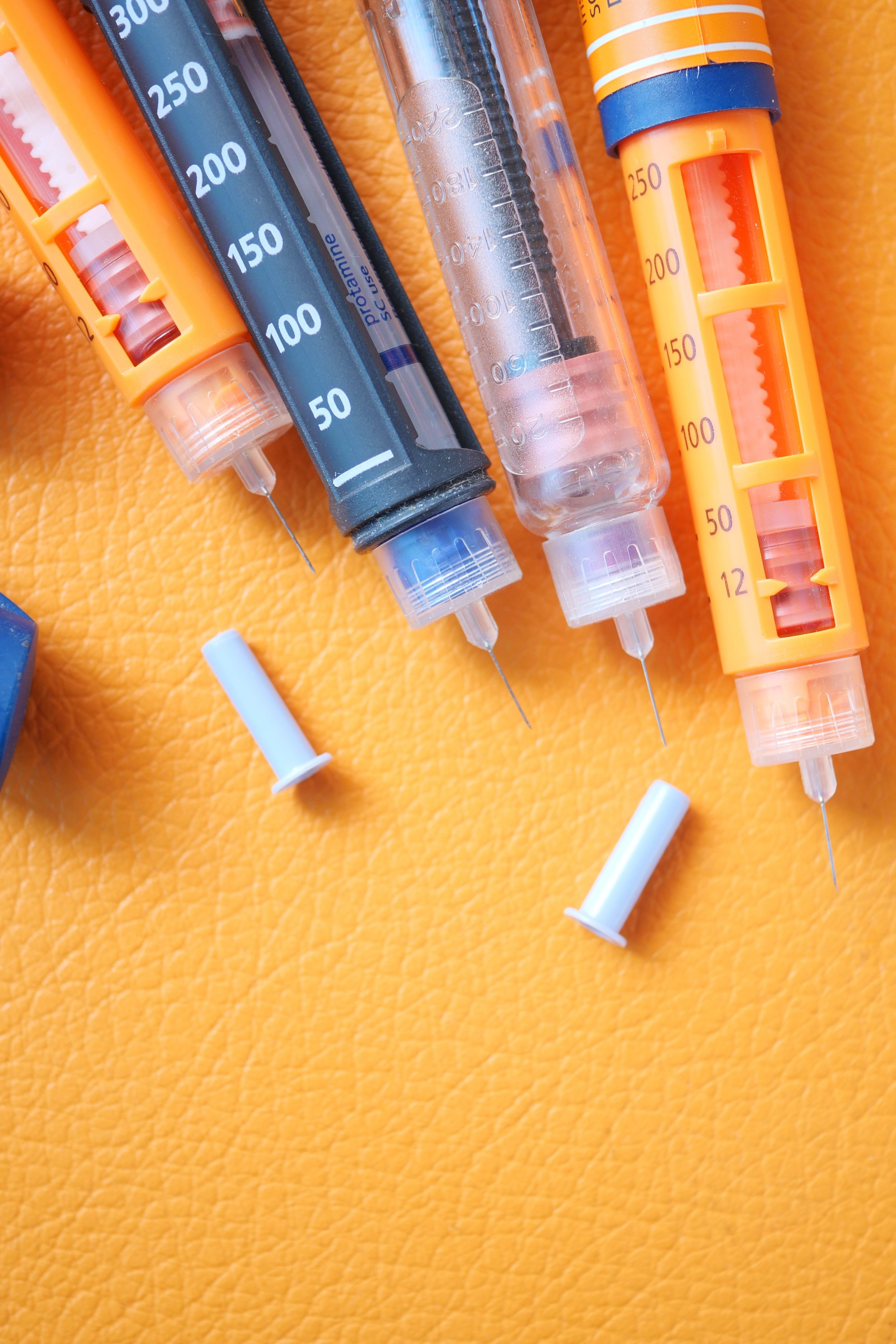 Several syringes and a needle cap on a bright orange textured surface.