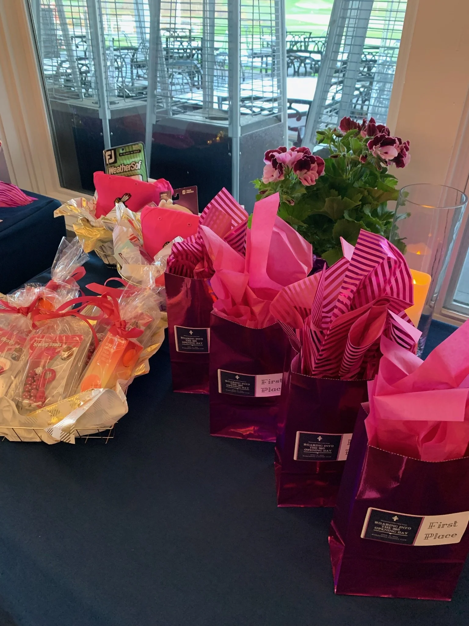 Table with pink and purple gift bags, a pink pillow, a small potted plant with pink flowers, and assorted wrapped candies. In the background, a large window with outdoor patio furniture can be seen.