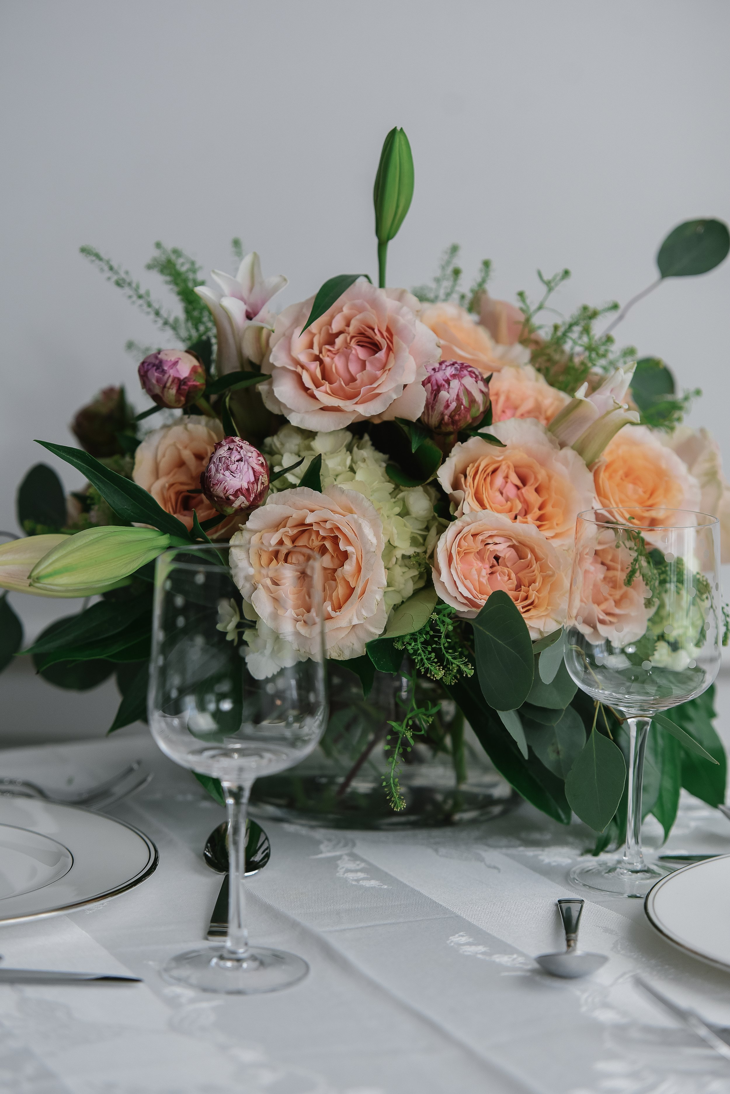 Elegant table setting with a floral centerpiece, wine glasses, and fine china, featuring a white tablecloth.