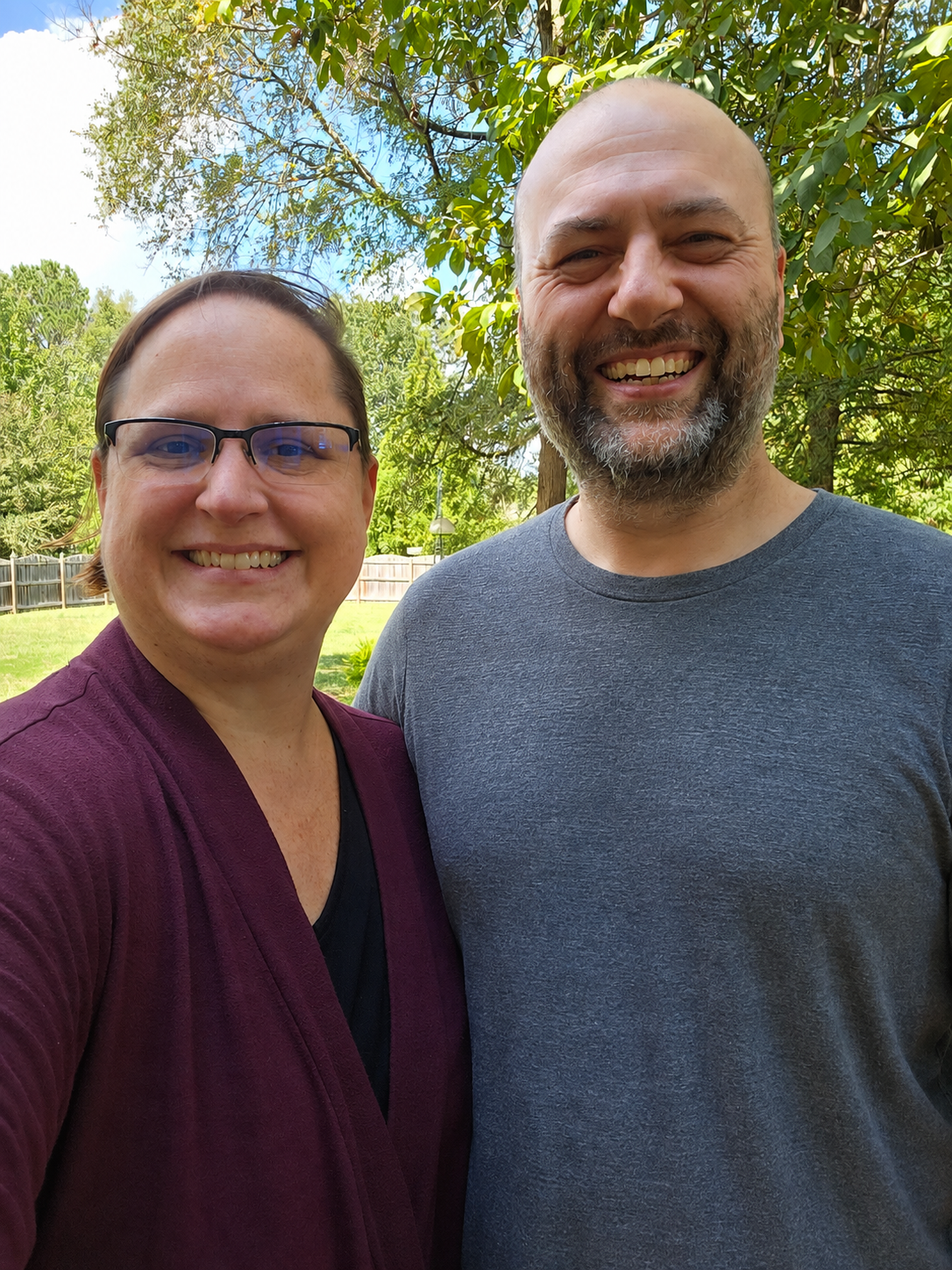woman with short brown hair and glasses standing next to a bearded man in a gray shirt