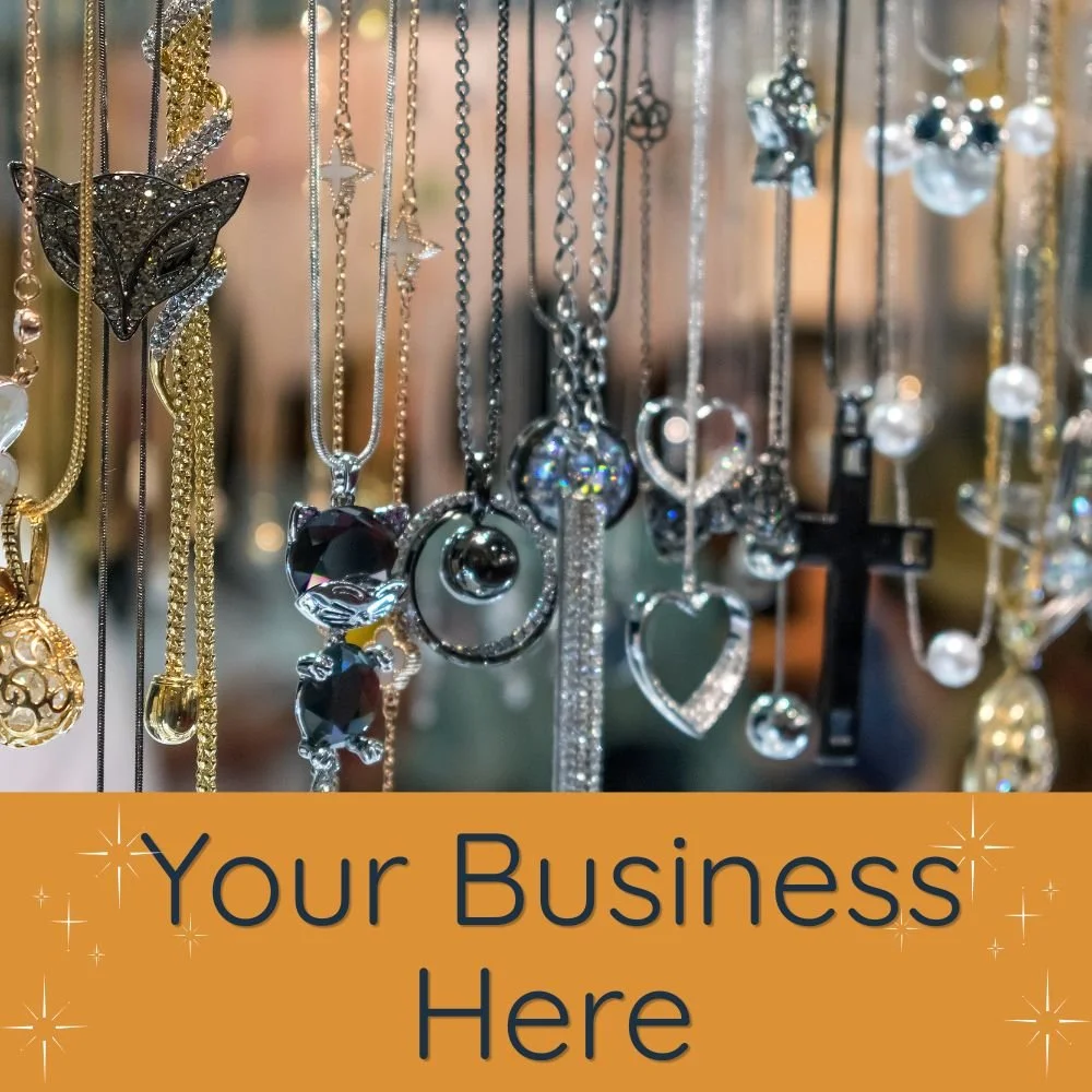 A display of various jewelry necklaces hanging from hooks, including pendants in the shapes of hearts, crosses, and stars, with a text overlay that reads "Your Business Here" on an orange background at the bottom.
