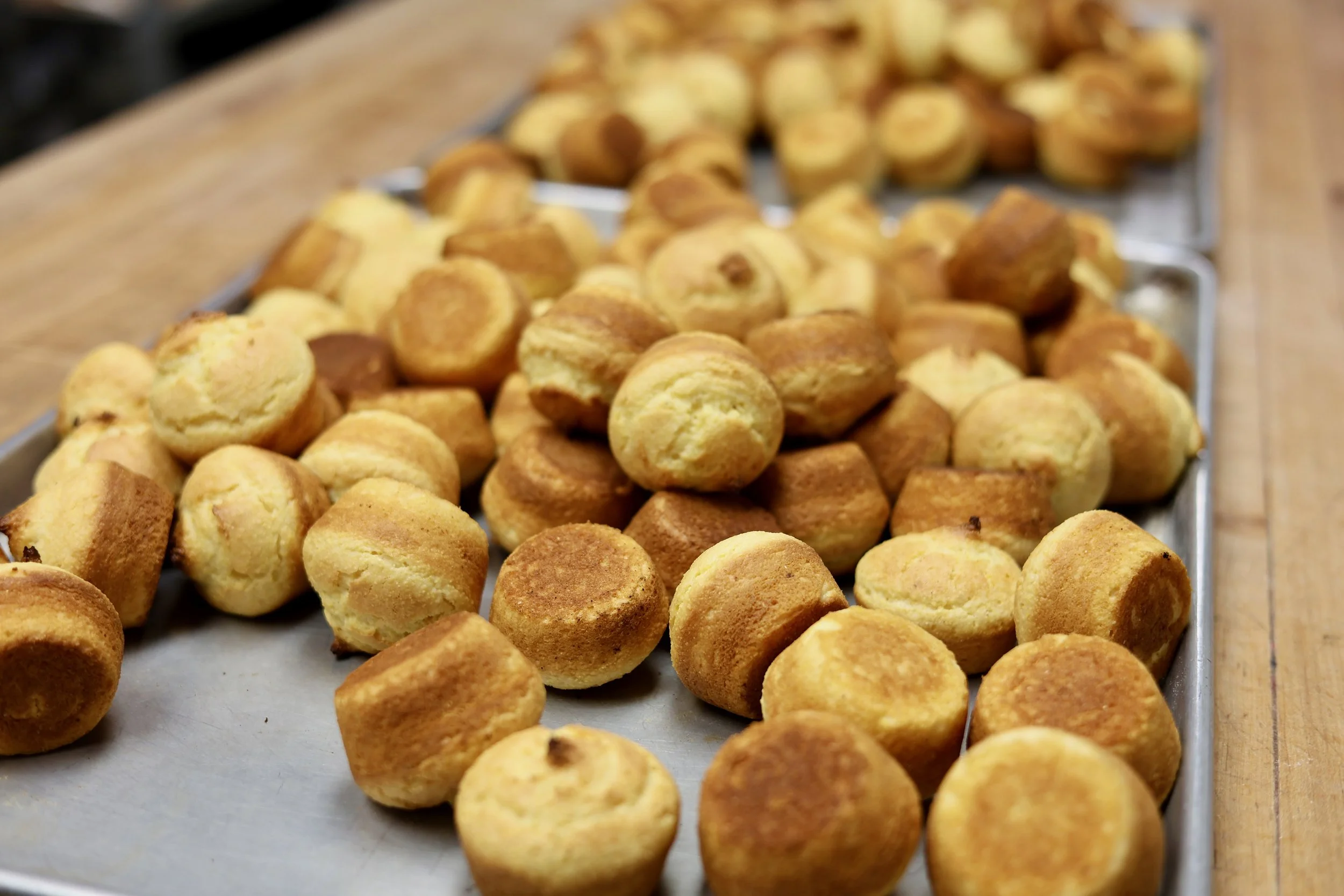 Close-up of small, round, baked snacks resembling cheese balls or cheese bread, piled on a tray on a wooden surface.
