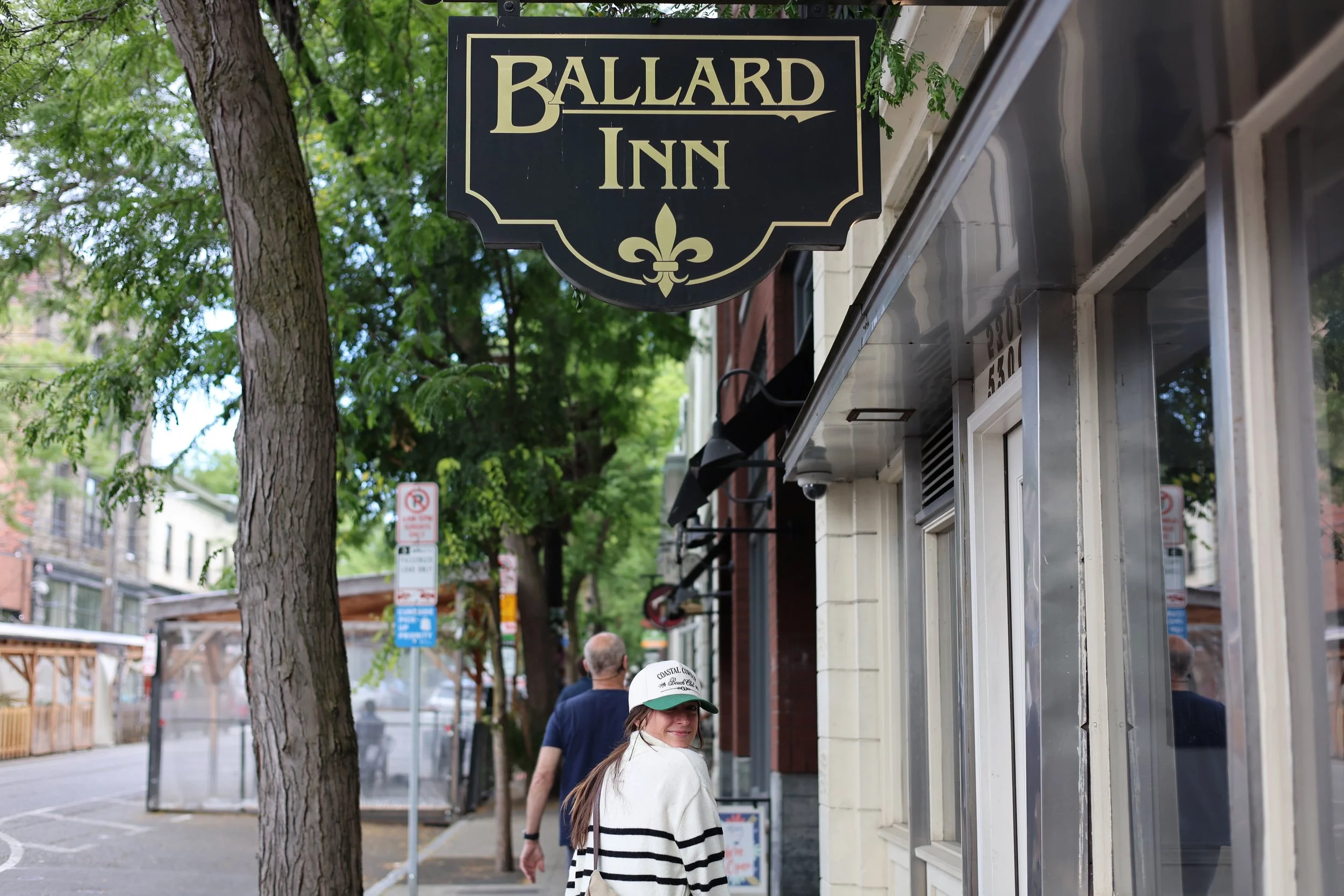 People walking on a city street near a building with a sign that reads 'Ballard Inn.'