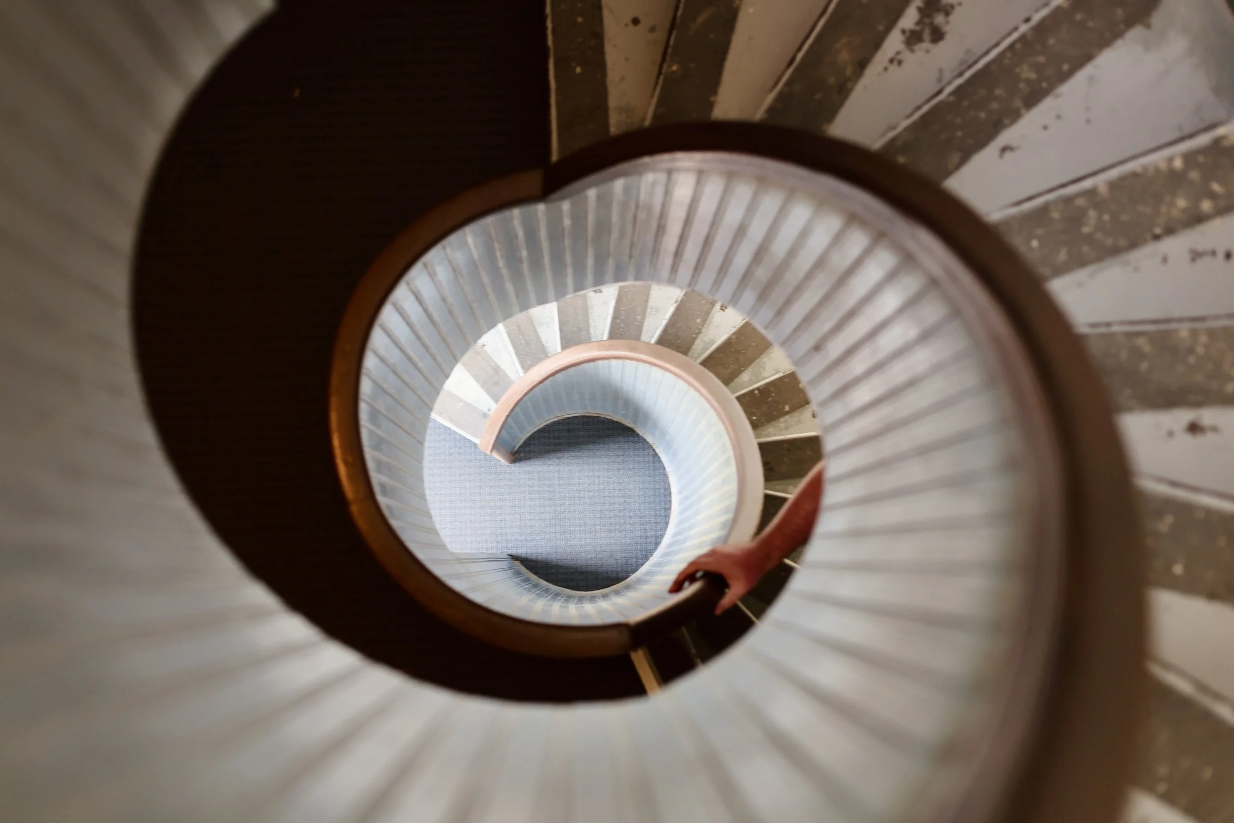 View looking down a spiral staircase with metal railings and steps, descending into a dimly lit space.