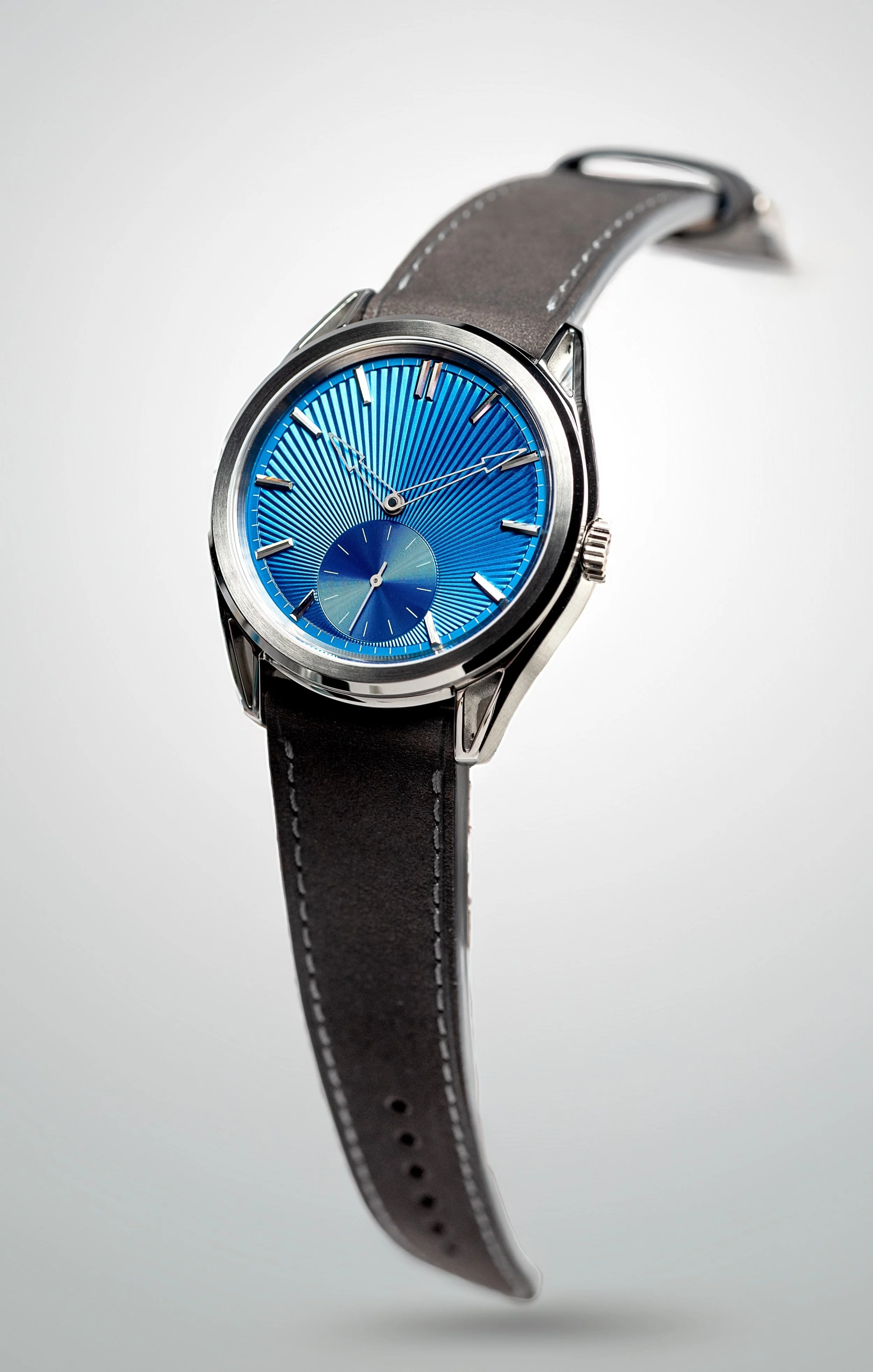 A wristwatch with a blue textured dial, silver-tone hands, and a grey leather strap with grey stitching, set against a plain white background.