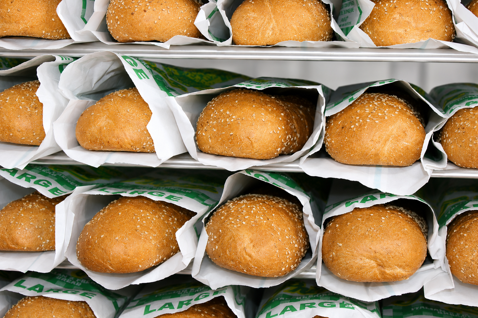 Multiple sesame seed sandwich buns on store shelves in paper wrappers.