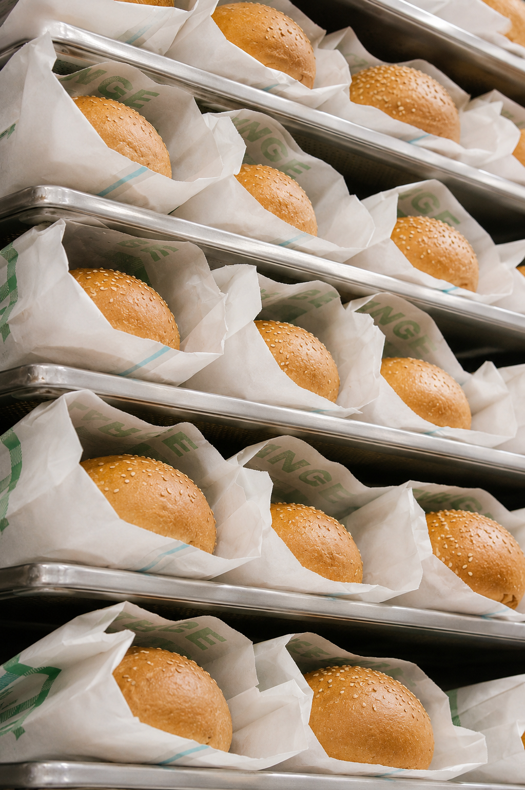 Multiple trays of hamburger buns wrapped in white paper with green text, stacked in rows.