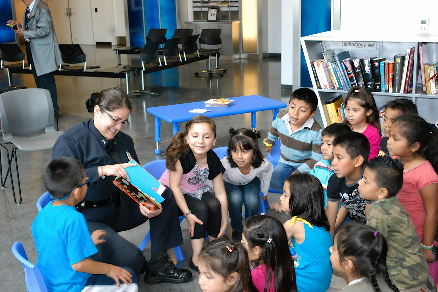 A female officer reading a book to a group of children in a library or community center
