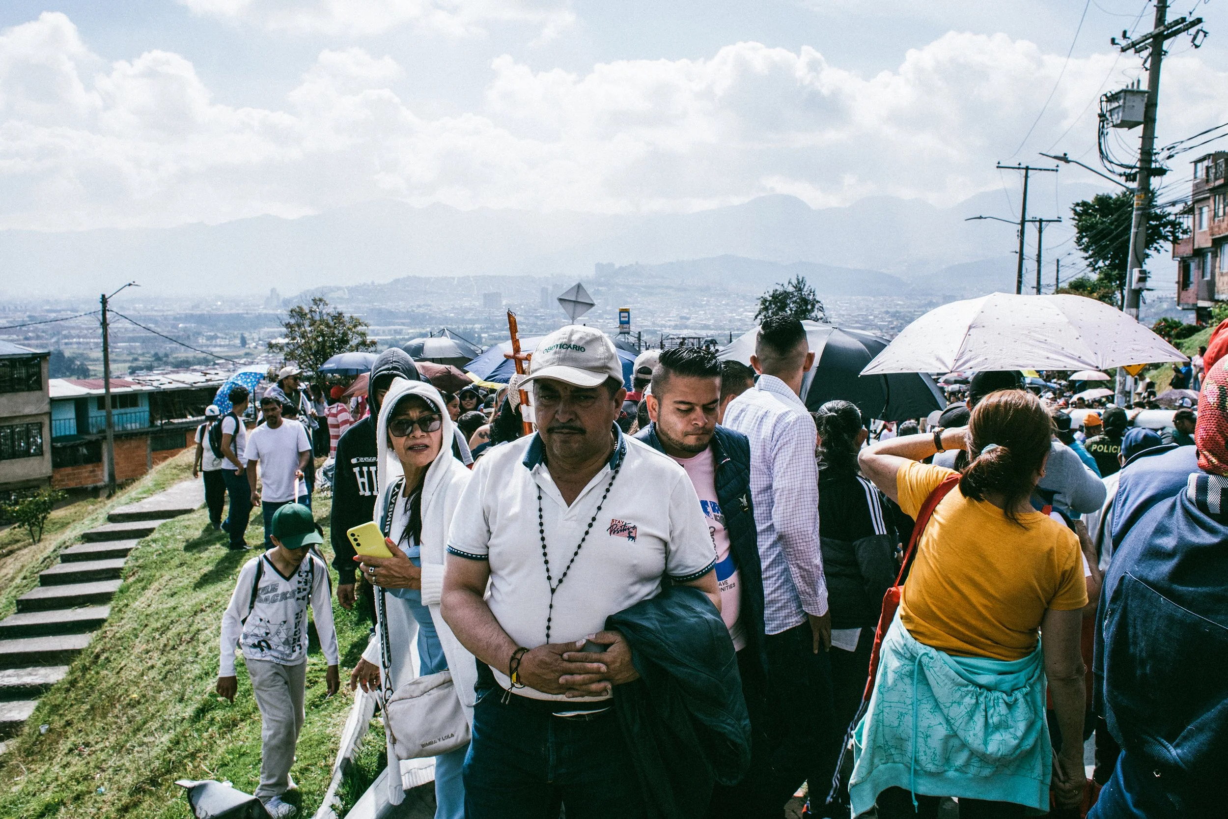 Multitud de personas caminando juntas en una marcha o manifestación al aire libre, con muchos paraguas y en un entorno urbano con colinas y montañas de fondo.