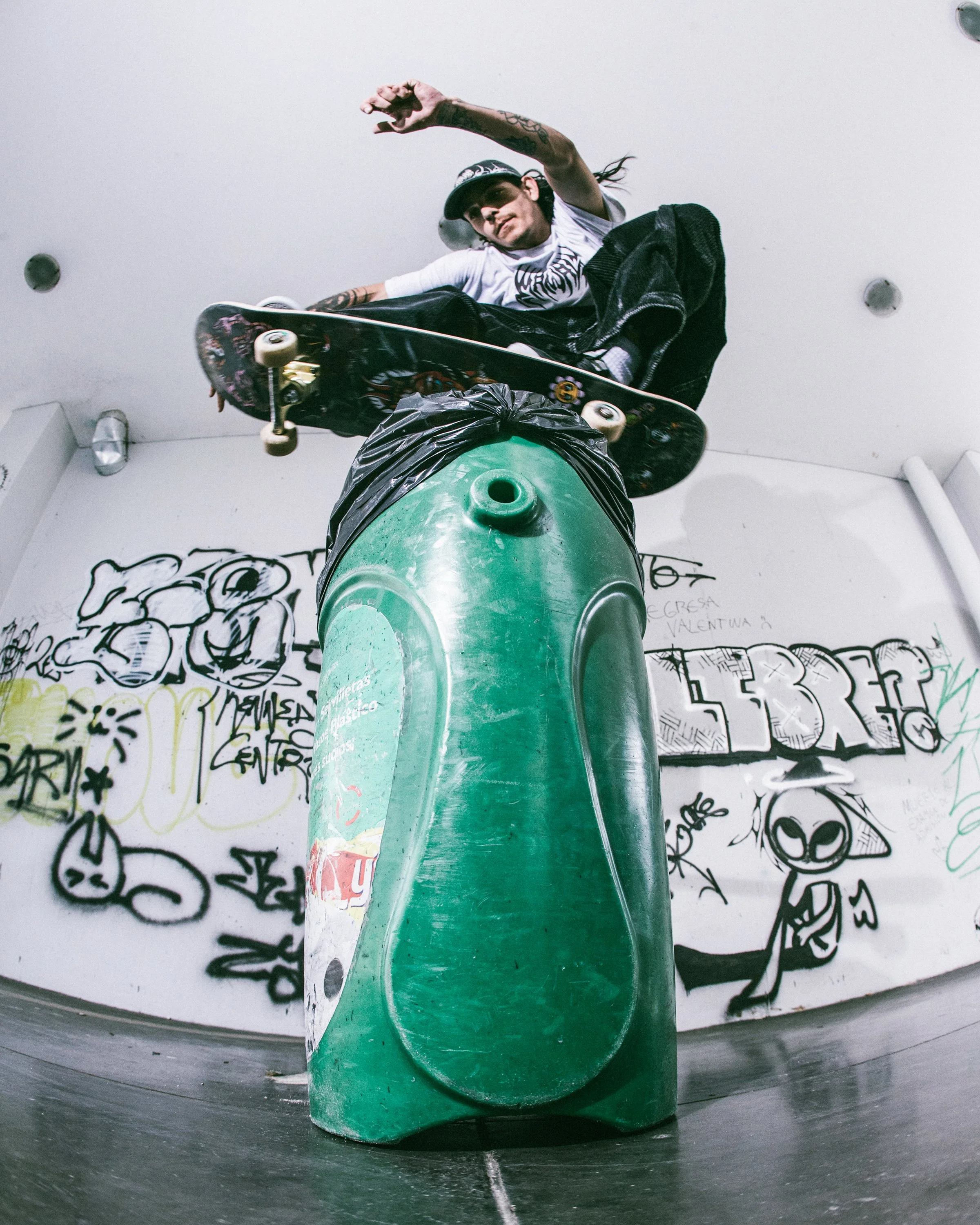 Una persona en un skate performing un truco en un espacio con paredes decoradas con graffiti