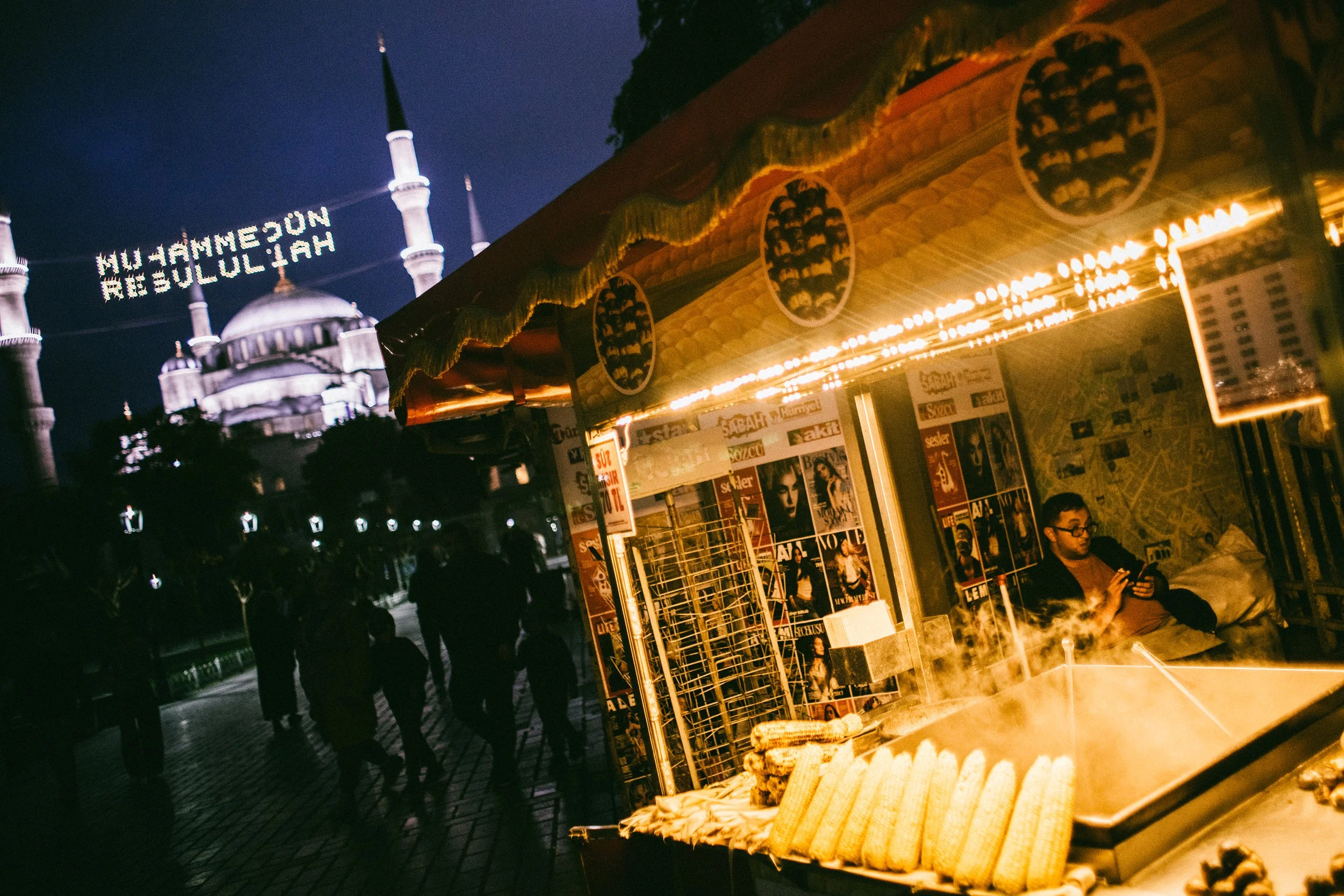 Vendedora en puesto de comida en la noche, con un camello en referencia a un marco y la mezquita Sultan Ahmed en Estambul al fondo.