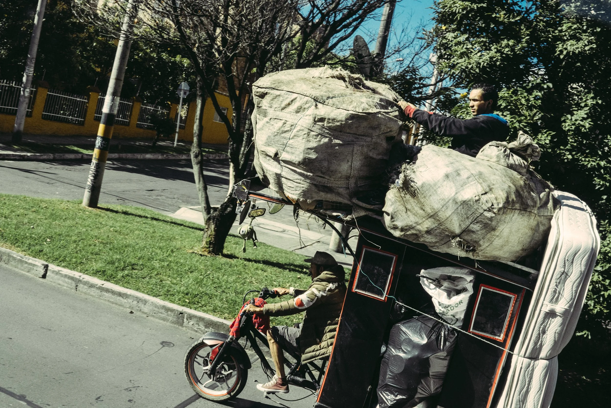Un hombre en una motocicleta transporta una gran cantidad de bolsas y objetos cubiertos con tela en una calle