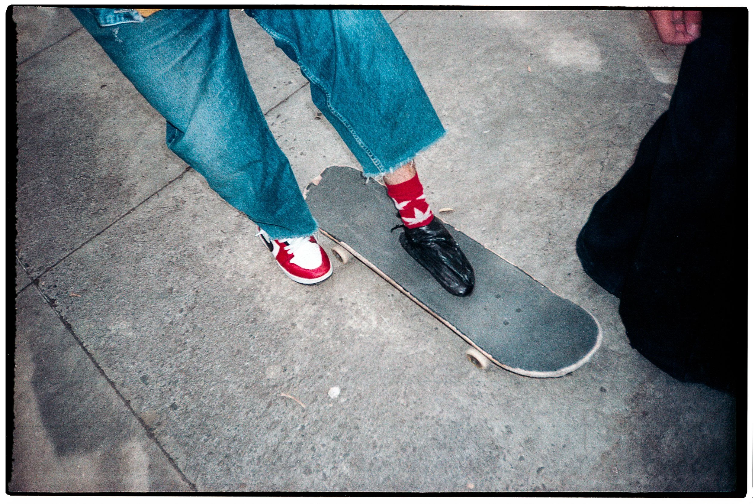 Persona en jeans con patineta en concreto, mostrando sus zapatos deportivos, uno rojo y blanco y otro negro y blanco.