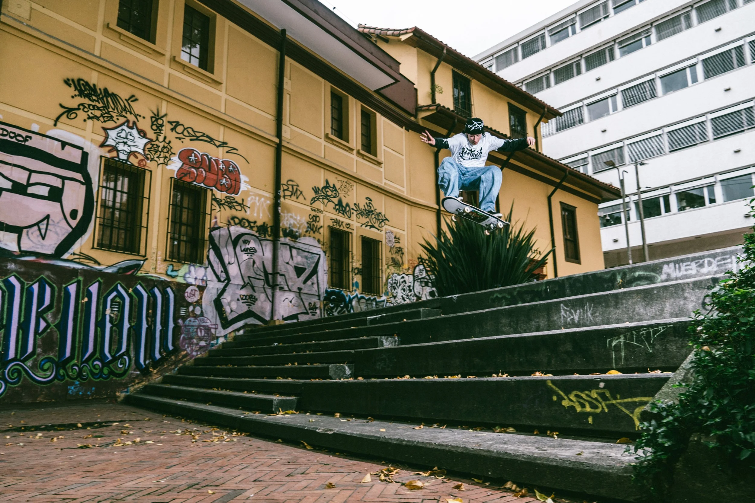 Joven haciendo trucos de skate en un parque con escaleras de cemento y arte urbano en las paredes.