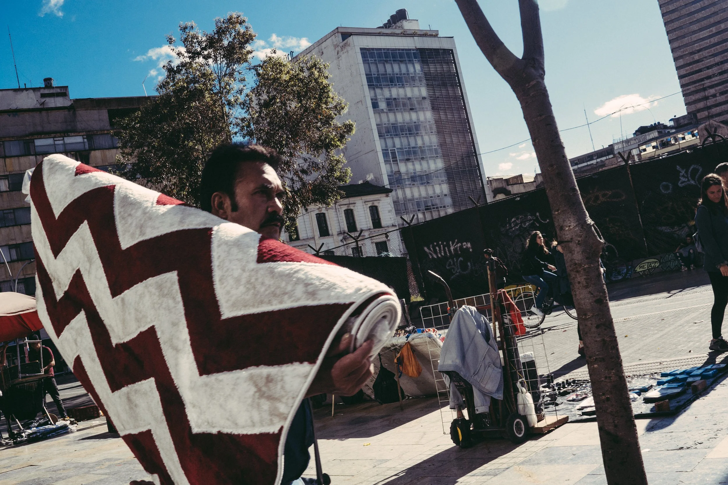Persona vendiendo ropa en un puesto al aire libre con edificios altos al fondo.