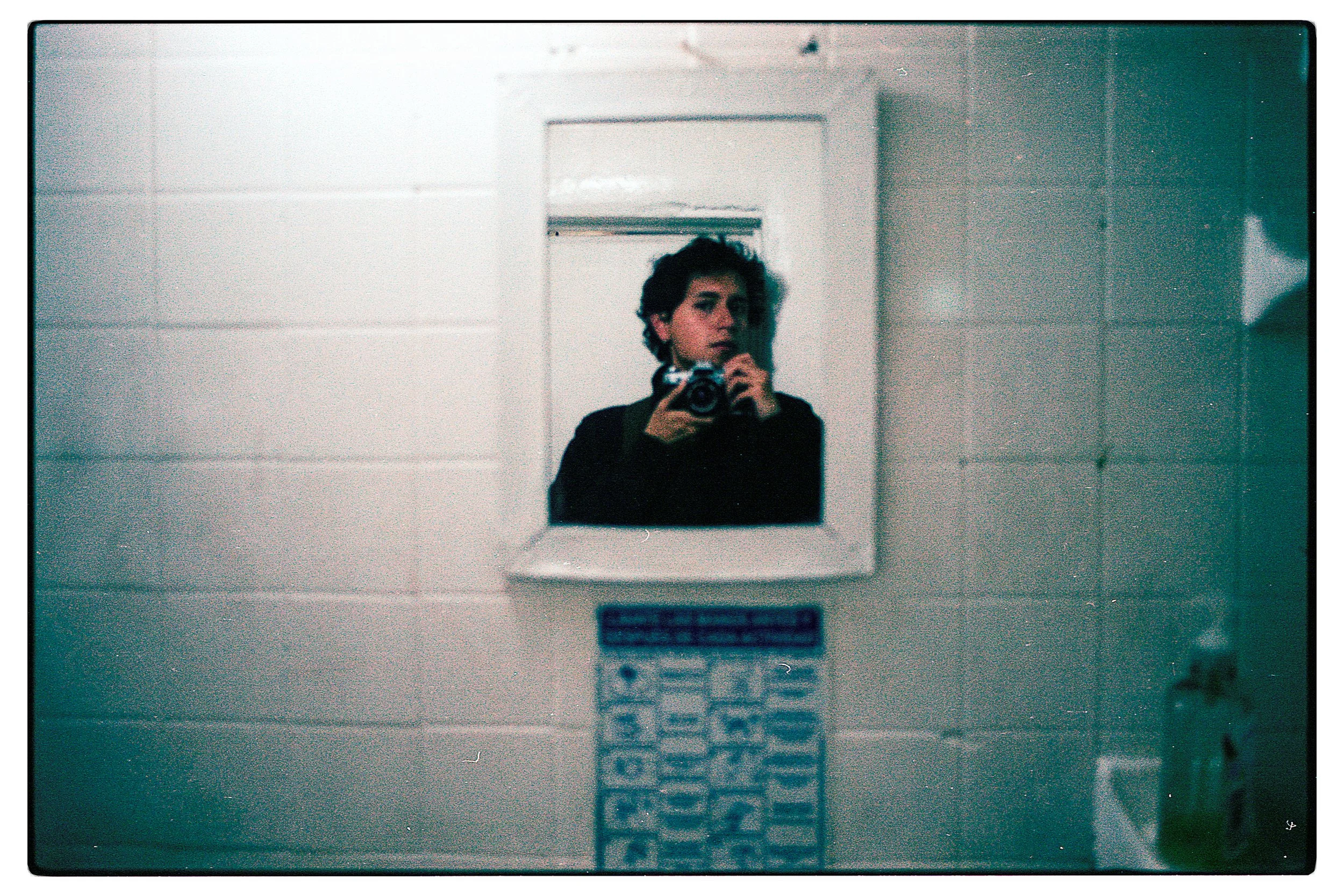 Espejo retrovisor en una habitación con una persona tomando una selfie en el espejo, se observa un teléfono en su mano y un fondo con paredes blancas y una puerta.
