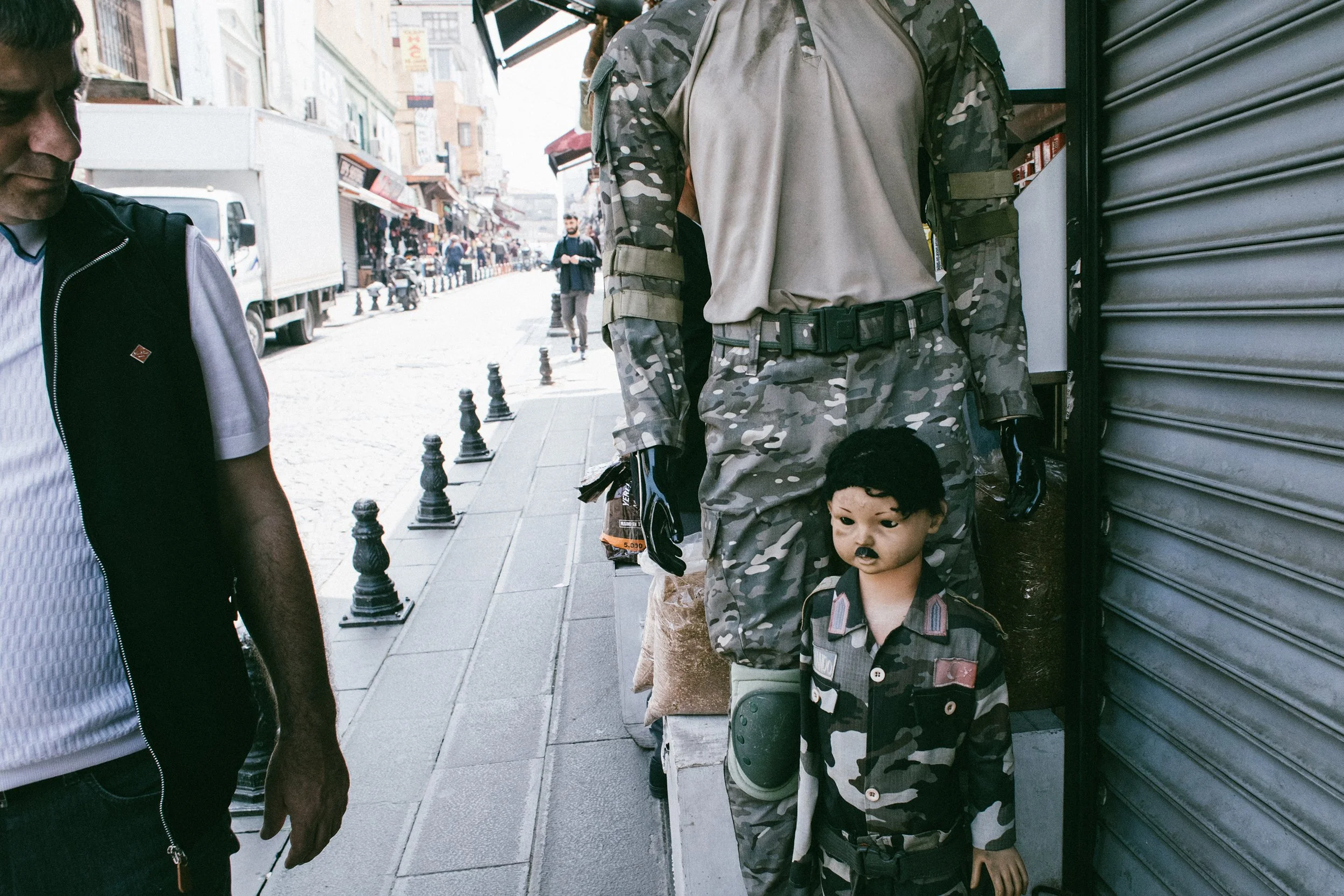 Estatua de un soldado con uniforme de camuflaje y un niño con ropa de camuflaje en la calle. Hay tiendas y personas en el fondo.