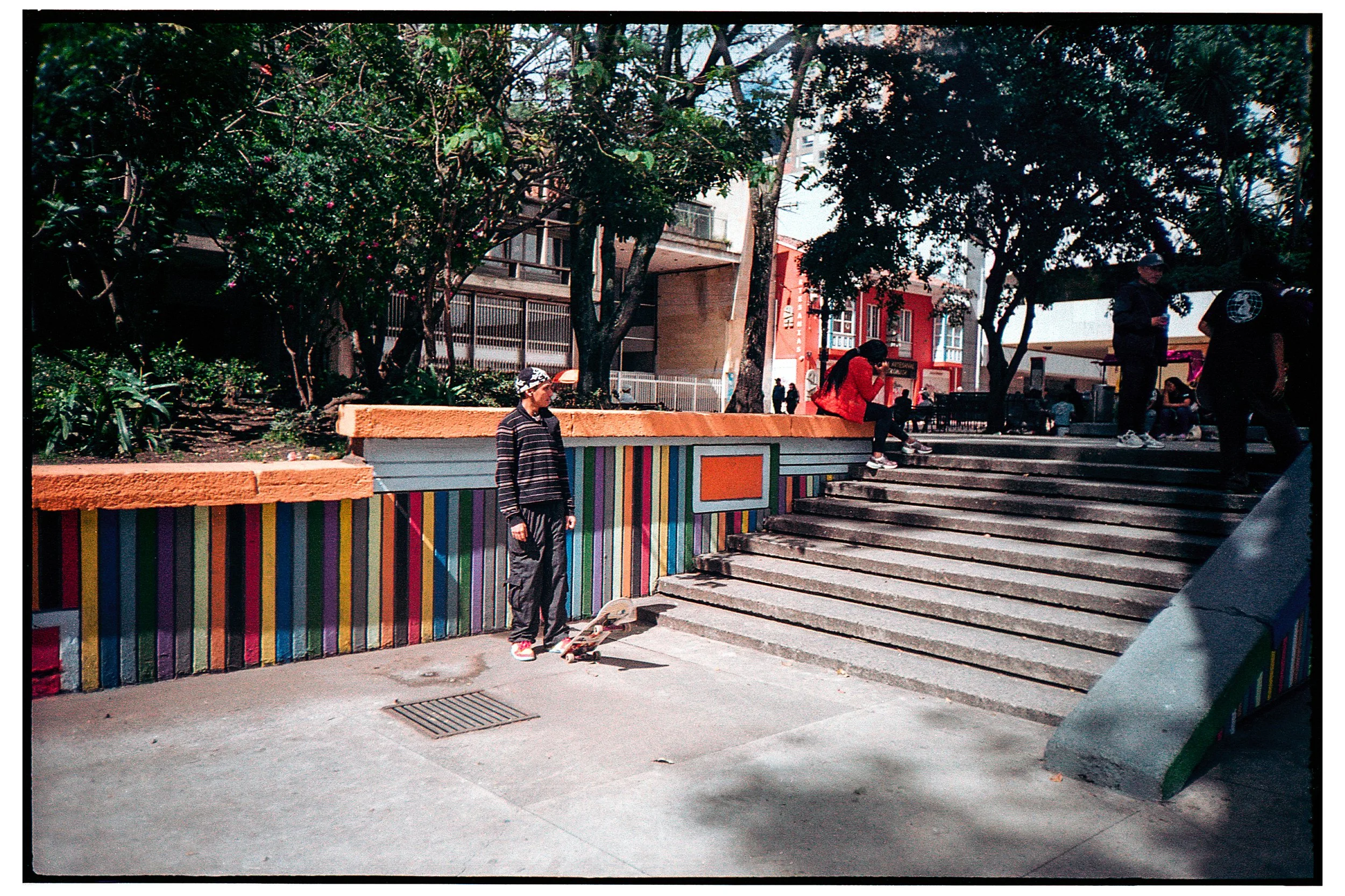 Escalones con pared decorativa de colores vibrantes en la base, varias personas en el lugar, árboles y edificios en el fondo.