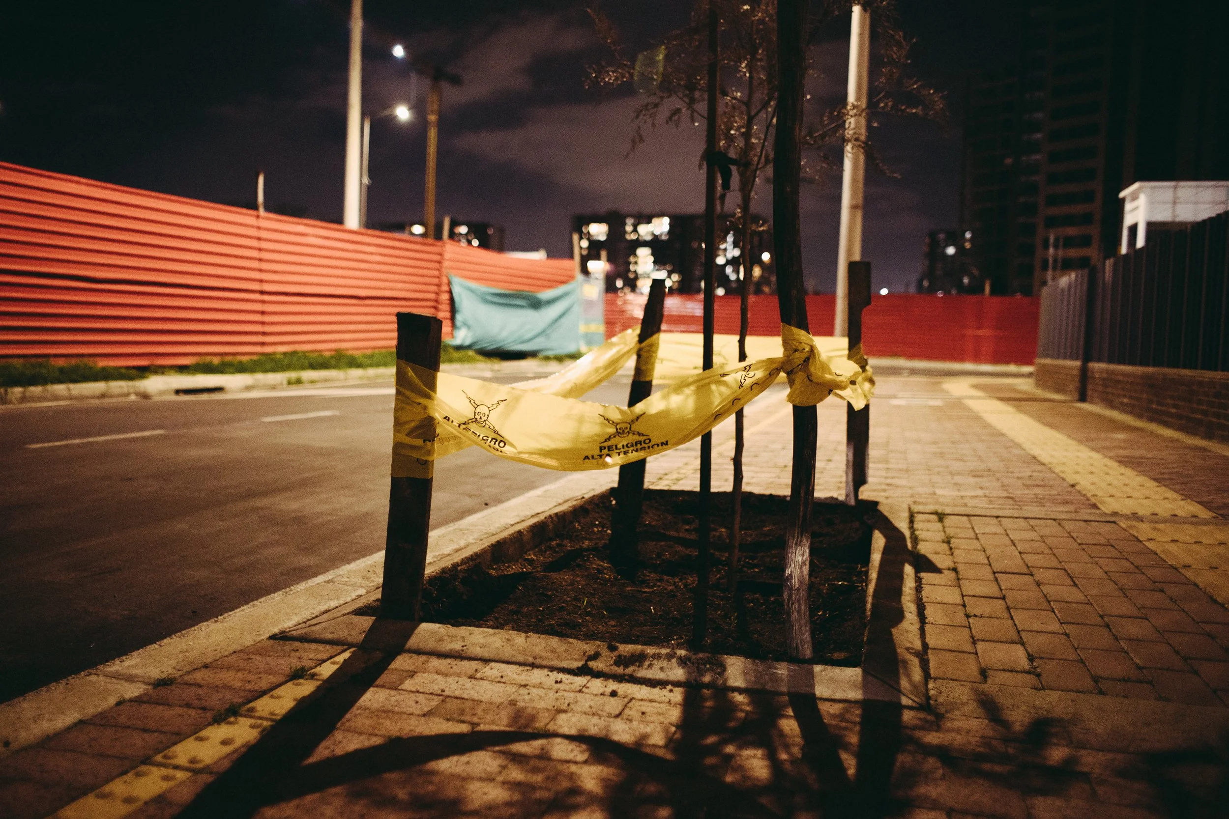 Señal de advertencia de peligro en amarillo en una cerca de protección en la noche, con una calle vacía y edificios en el fondo.