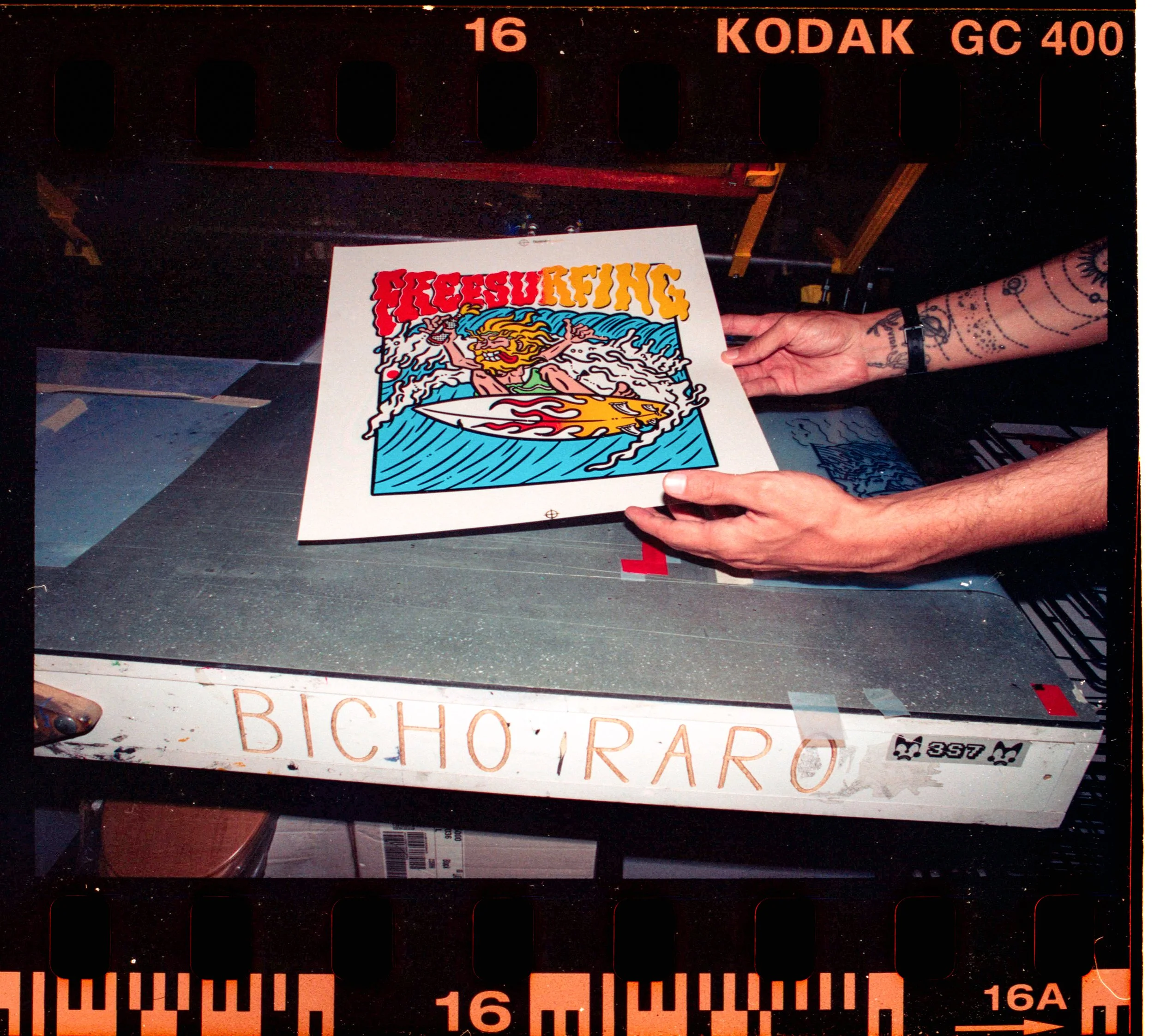 Persona sosteniendo un cartel con diseño colorido y letras en estilo retro, en un fondo oscuro con elementos de película y un rótulo de Kodak.