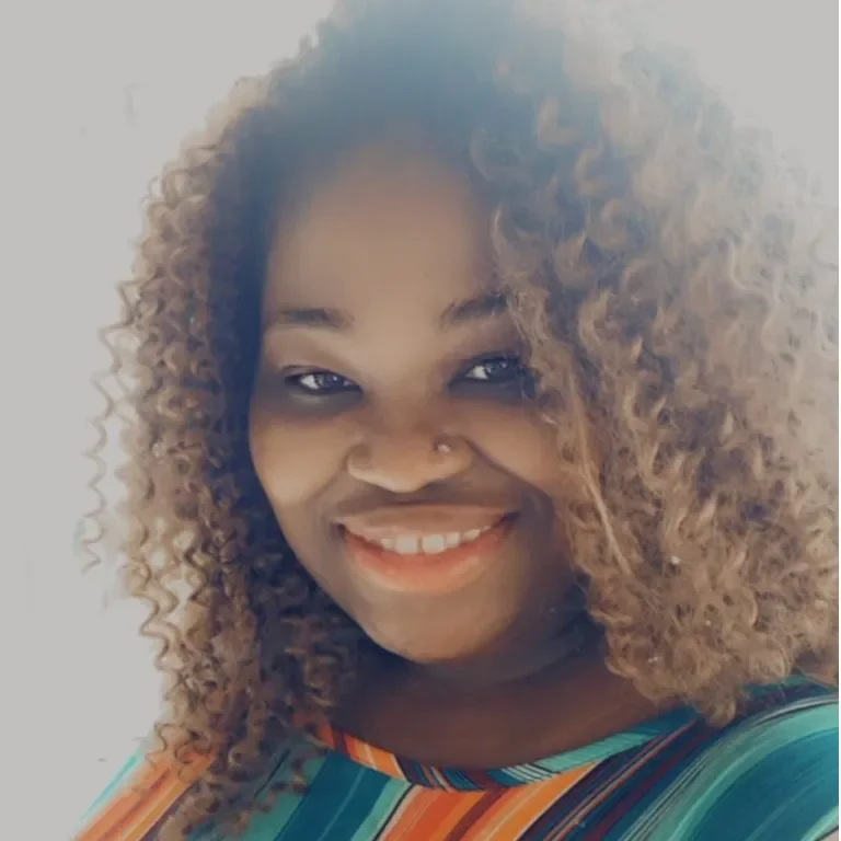 A woman with curly hair and a nose piercing smiling at the camera.
