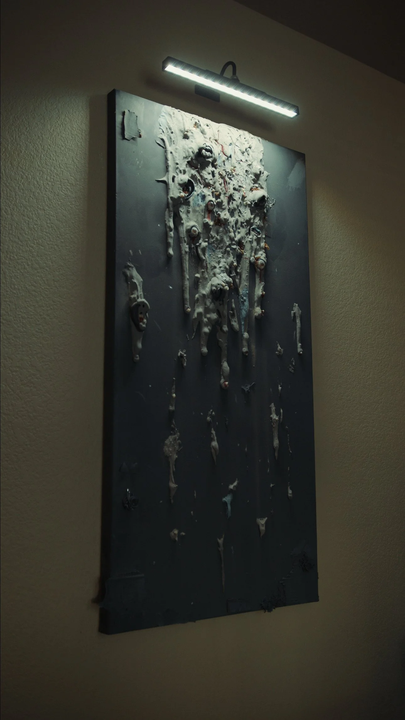 A textured artwork with white and black melted-looking elements on a dark background, illuminated by a horizontal overhead light.