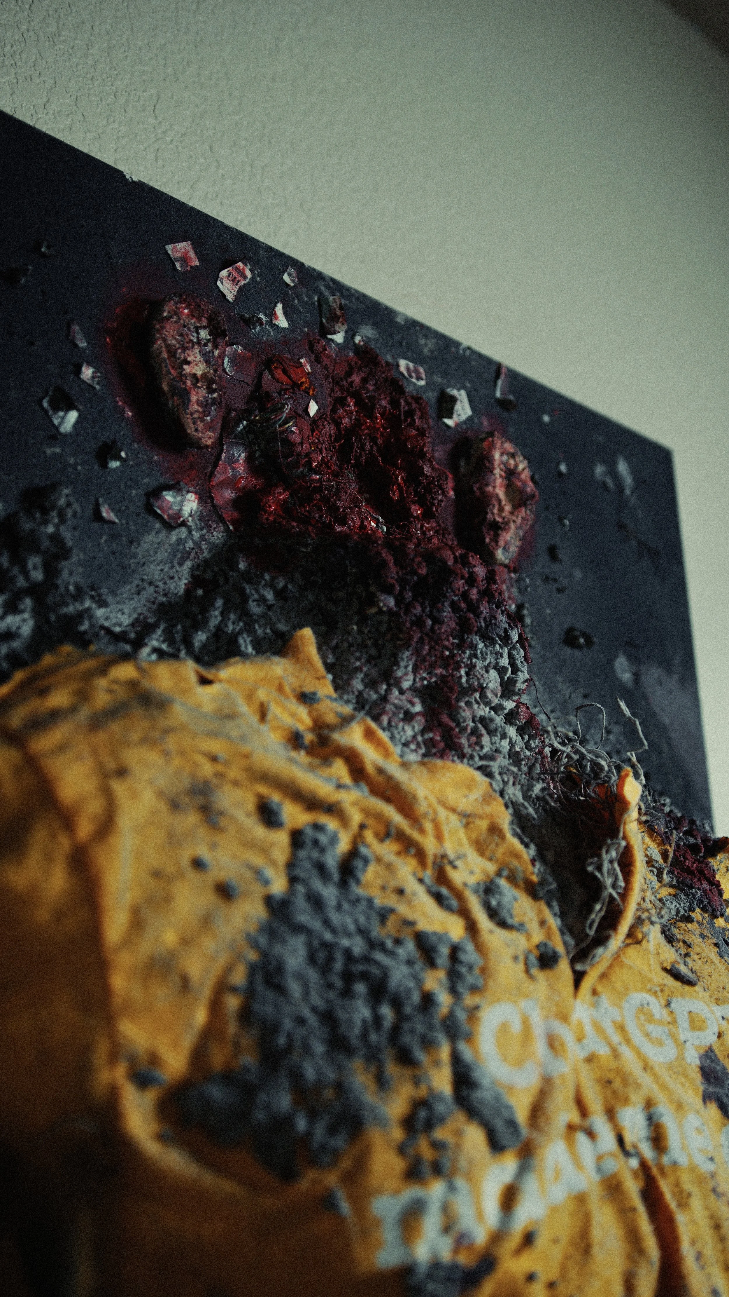 Close-up of a burnt and charred object, possibly food, with a black surface and reddish residue, alongside a yellowish object with partially visible white text.