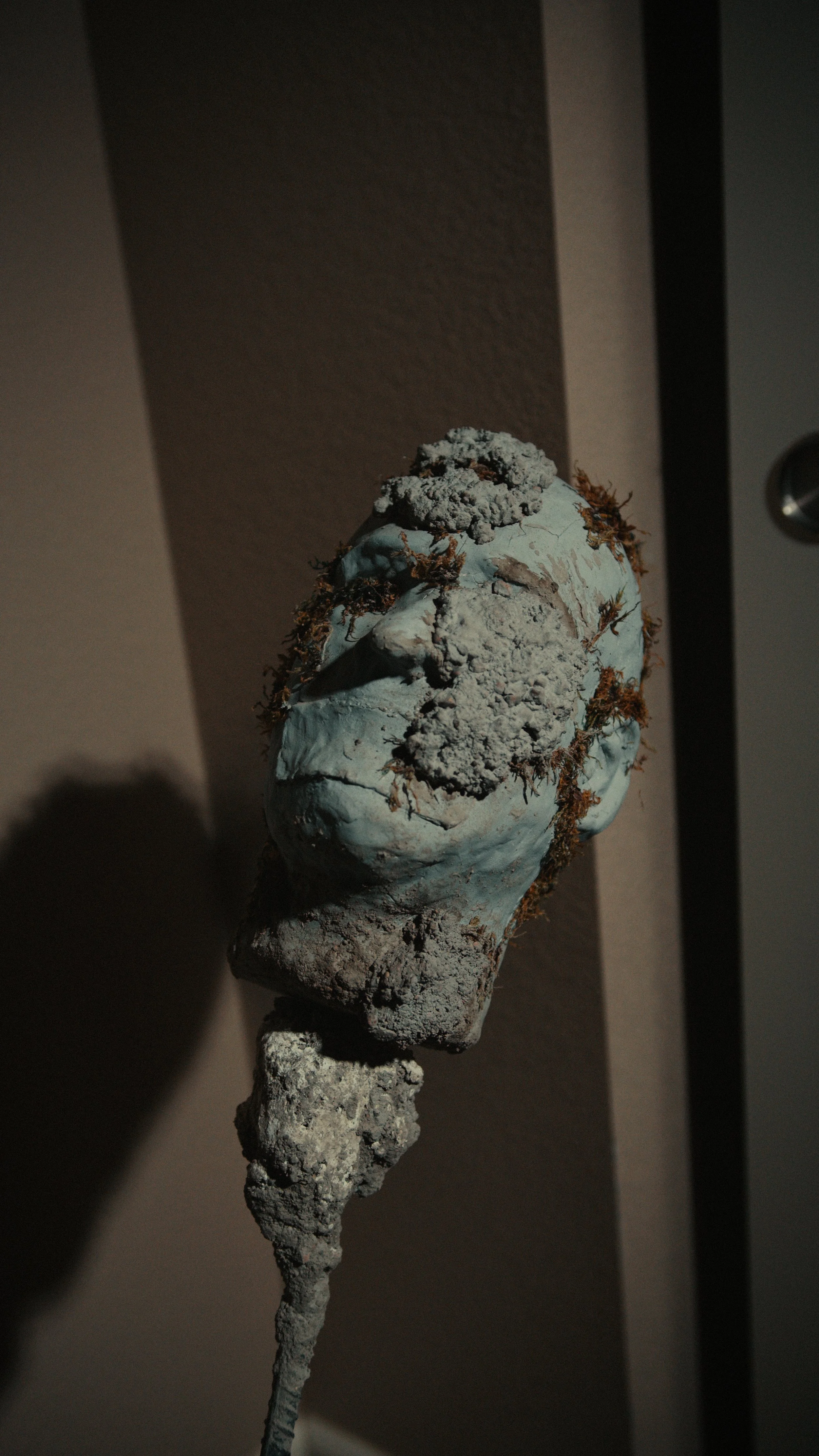 A weathered sculpture of a human head with a rough, cracked surface, multiple textures, and revealing signs of age and wear.