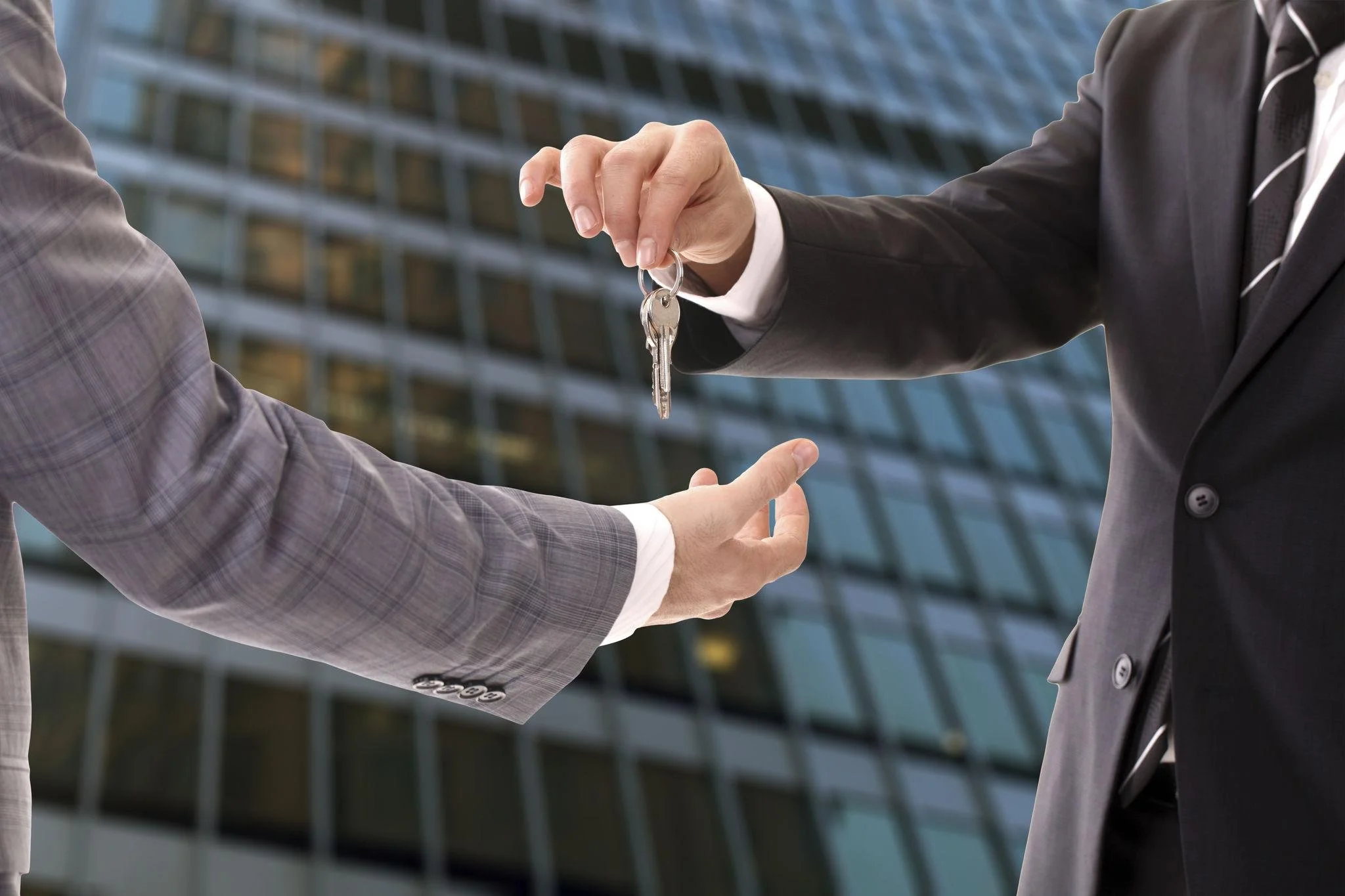 Two people exchanging keys in front of a modern office building.