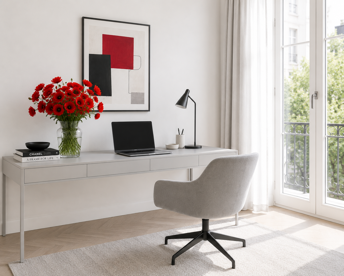 Home office with a light grey desk positioned against a white wall. A laptop sits on the desk beside a glass vase filled with red poppies.