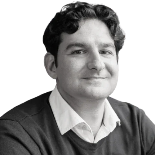 Black and white portrait of a man with curly dark hair, wearing a collared shirt and a sweater, smiling slightly.