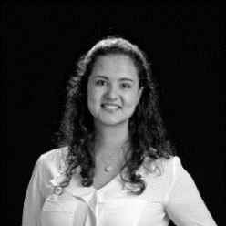 A young woman with curly hair and a white blouse smiling at the camera against a dark background.