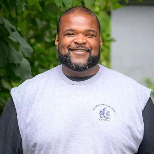A smiling man with a beard and short hair wearing a gray T-shirt outdoors.