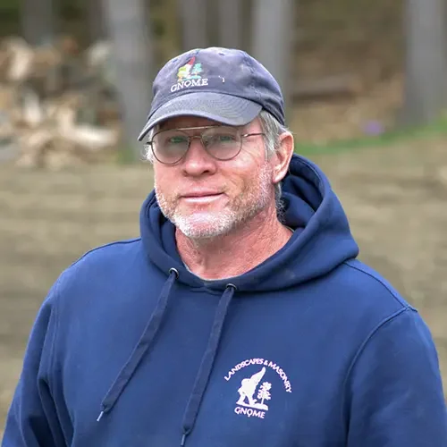 Man wearing glasses, a blue hoodie with a wildlife logo, and a cap with the Gnome logo, outdoors.