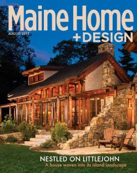 Magazine cover of Maine Home + Design, August 2015 issue, featuring a house with a stone chimney and wooden porch in an island landscape setting at dusk.