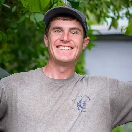 A young man smiling outdoors, wearing a gray T-shirt and a gray cap.