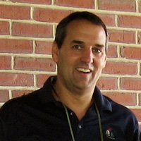 A man smiling and standing in front of a brick wall