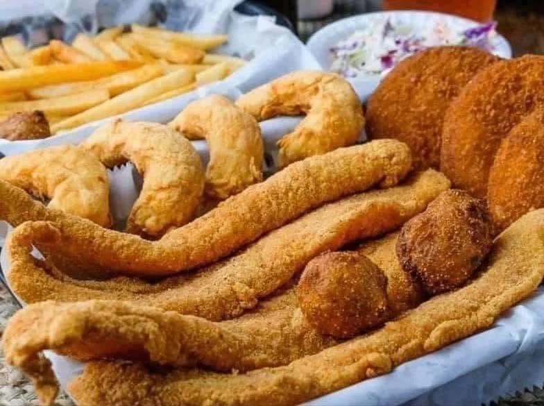 Basket of fried fish fillets, hush puppies, and French fries.