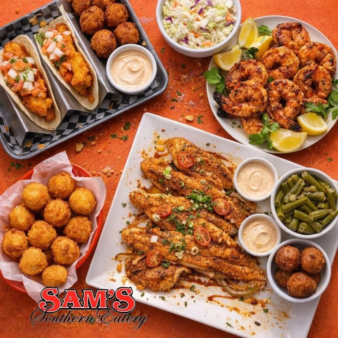 A table with various Southern dishes including fried fish topped with sliced tomatoes and green onions, roasted shrimp with lemon wedges, fried chicken nuggets, croquettes, hush puppies, cole slaw, and green beans, with a logo for Sam's Southern Eate